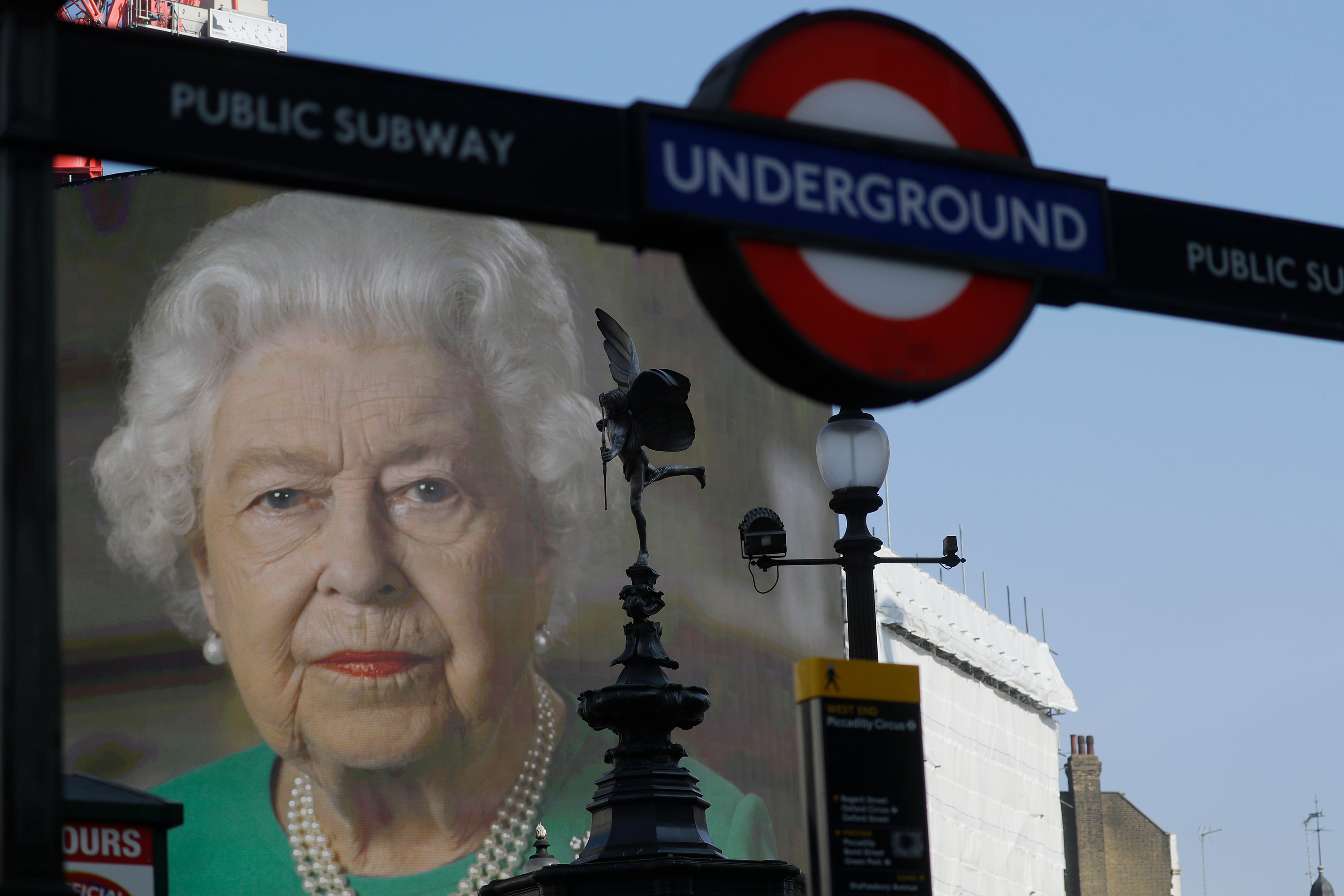 An image of Britain's Queen Elizabeth II and quotes from her historic television broadcast commenting on the coronavirus pandemic are displayed on a big screen behind the Eros statue and a London underground train station entrance at Piccadilly Circus in London on April 9.