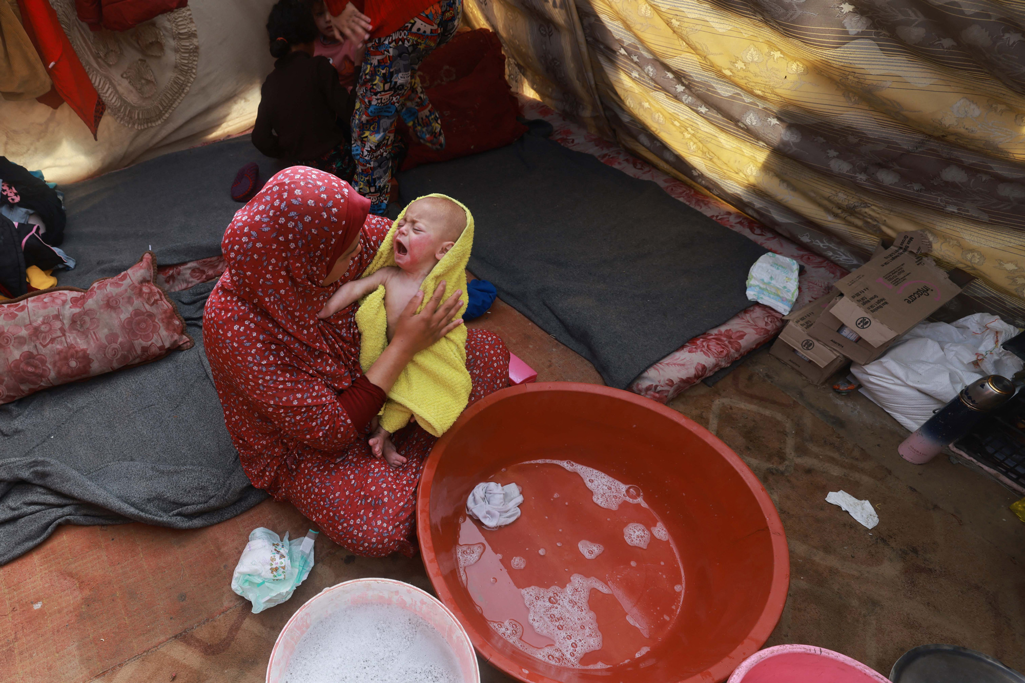 A woman dries a baby in a towel after giving it a bath, inside a tent at a camp for displaced Palestinians in Rafah, southern Gaza, on January 18.