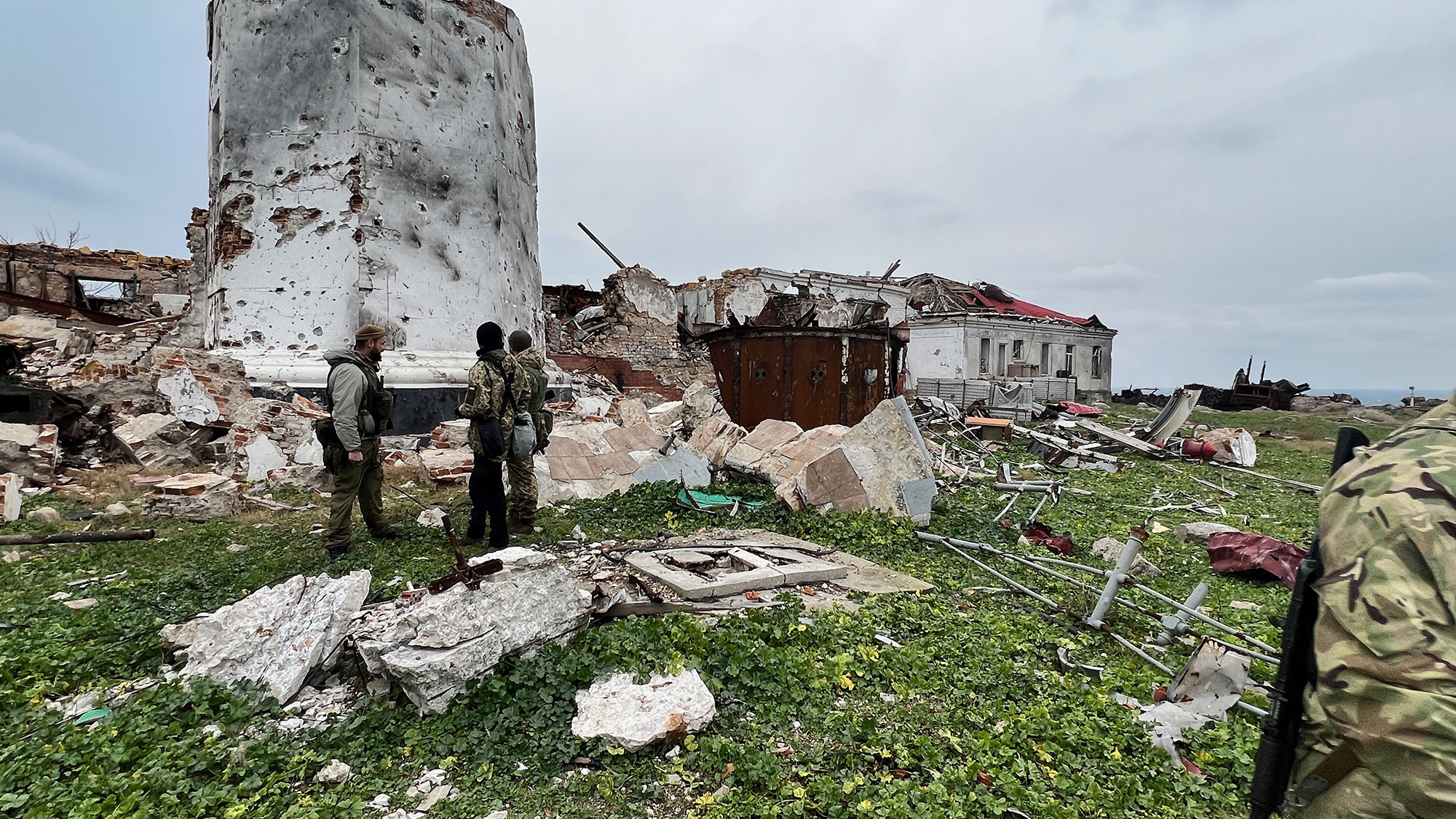 Ukrainian soldiers stand in front of the ruins of the lighthouse on Zmiinyi Island (also known as 
