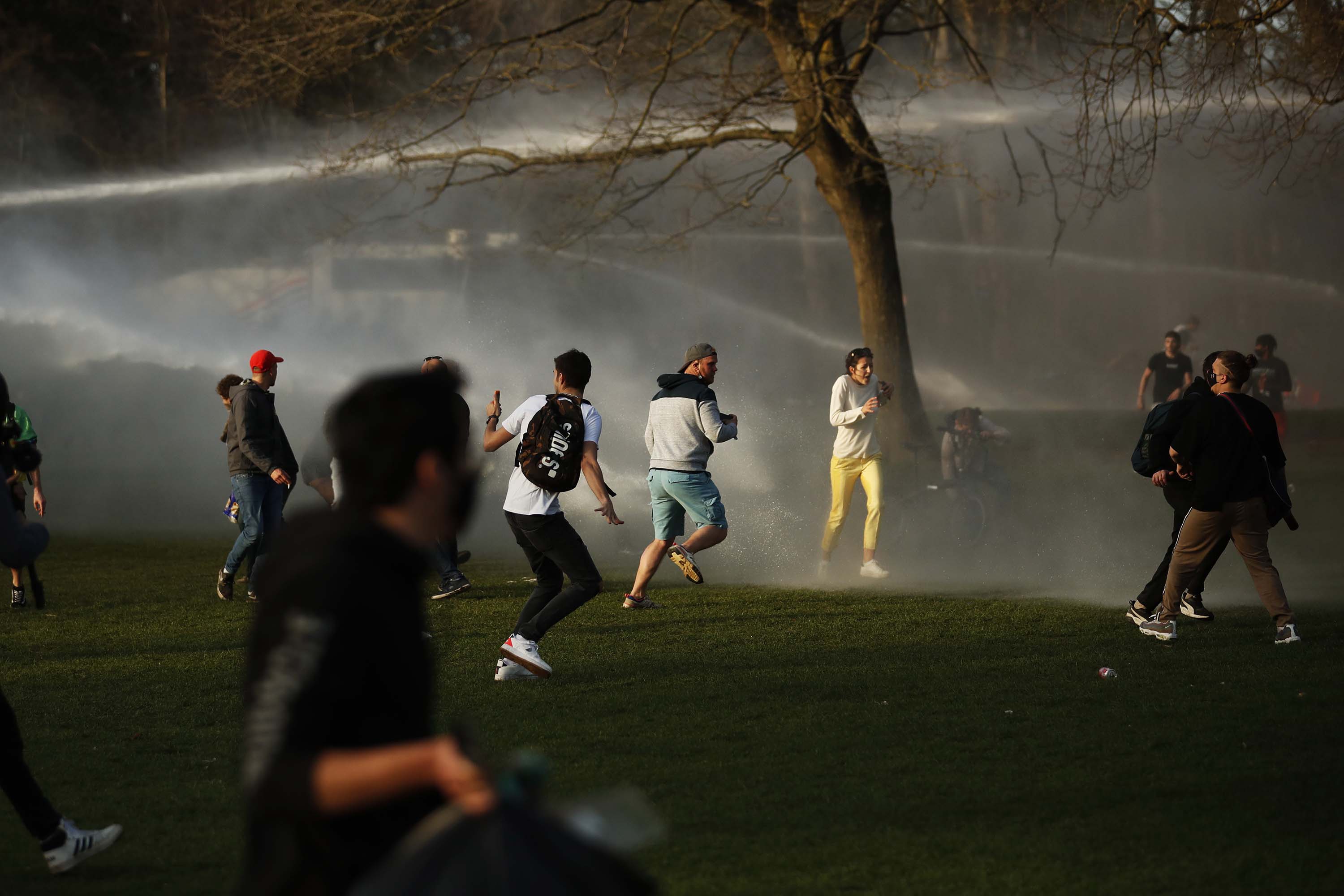 People scatter as police use a water cannon to disperse the crowd in Bois de la Cambre park.