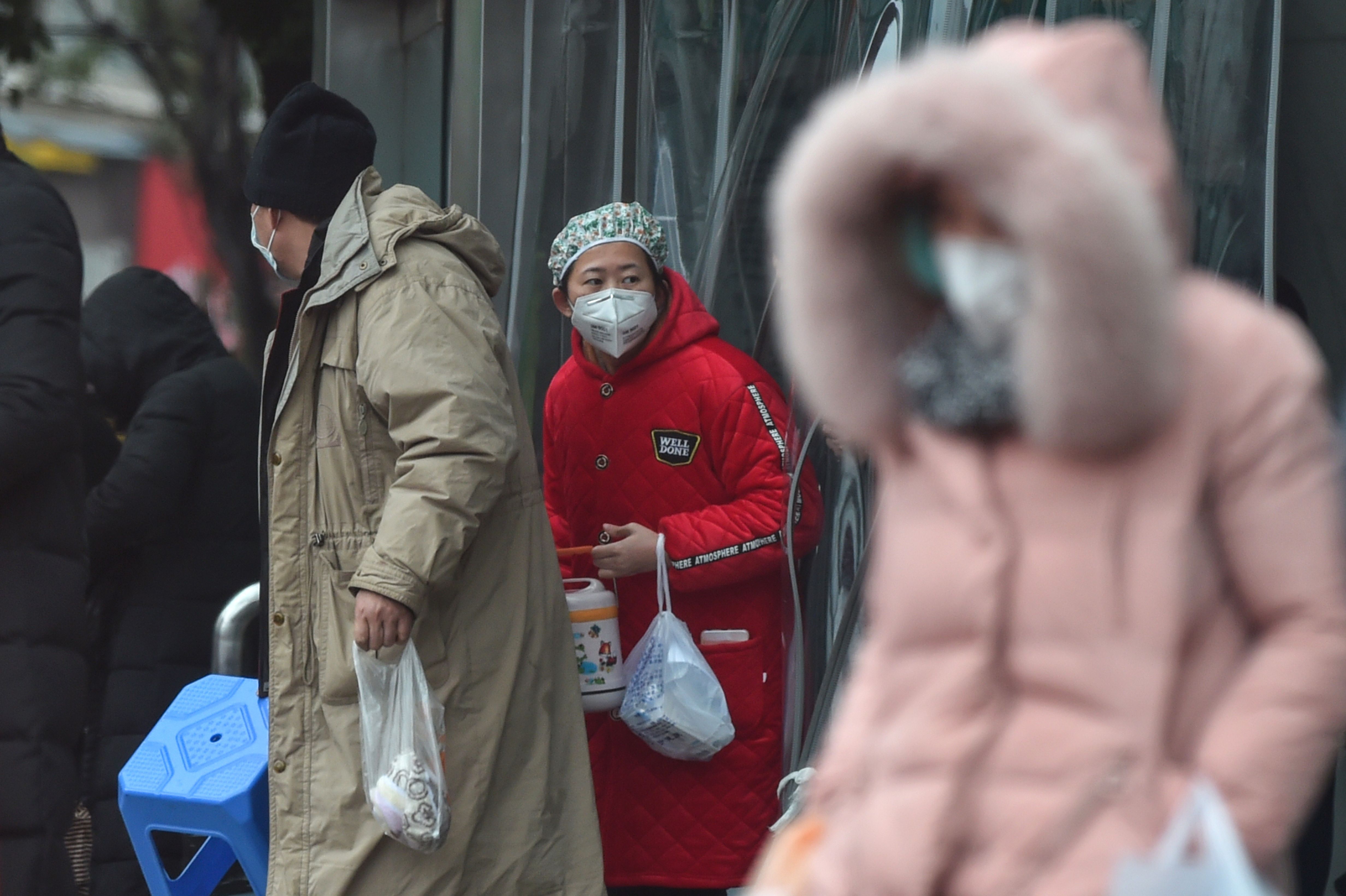 People wearing protective clothing to help stop the spread of a deadly virus stand on the street next to a hospital in Wuhan on January 24, 2020.