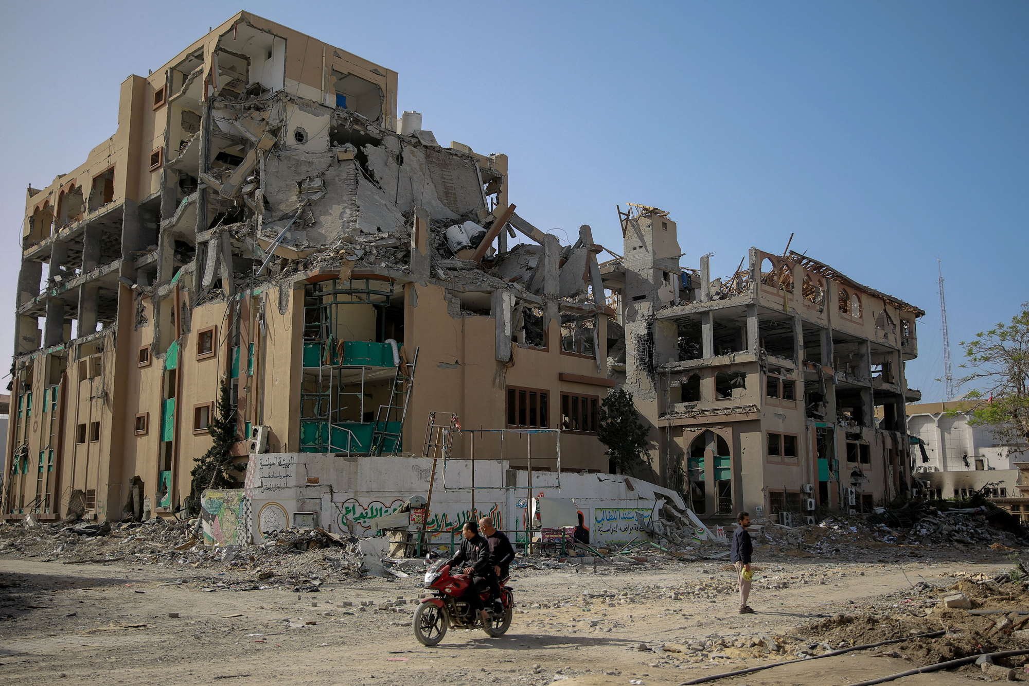Palestinians drive a motorcycle past the destroyed building of the Islamic University in Gaza City on November 26, 2023, on the third day of a truce between Israel and Hamas.