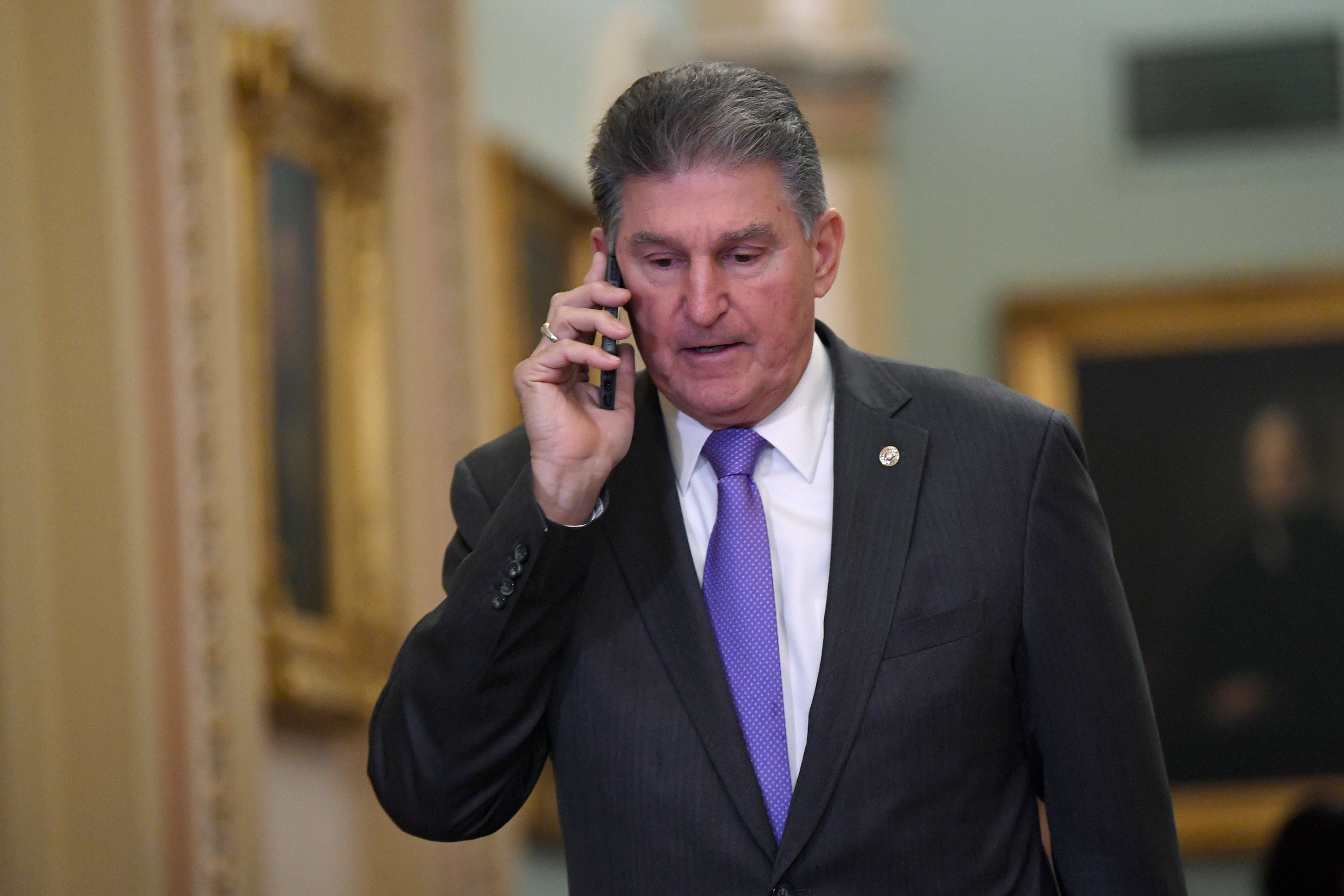 Sen. Joe Manchin talks on his phone Monday as he walks on Capitol Hill.