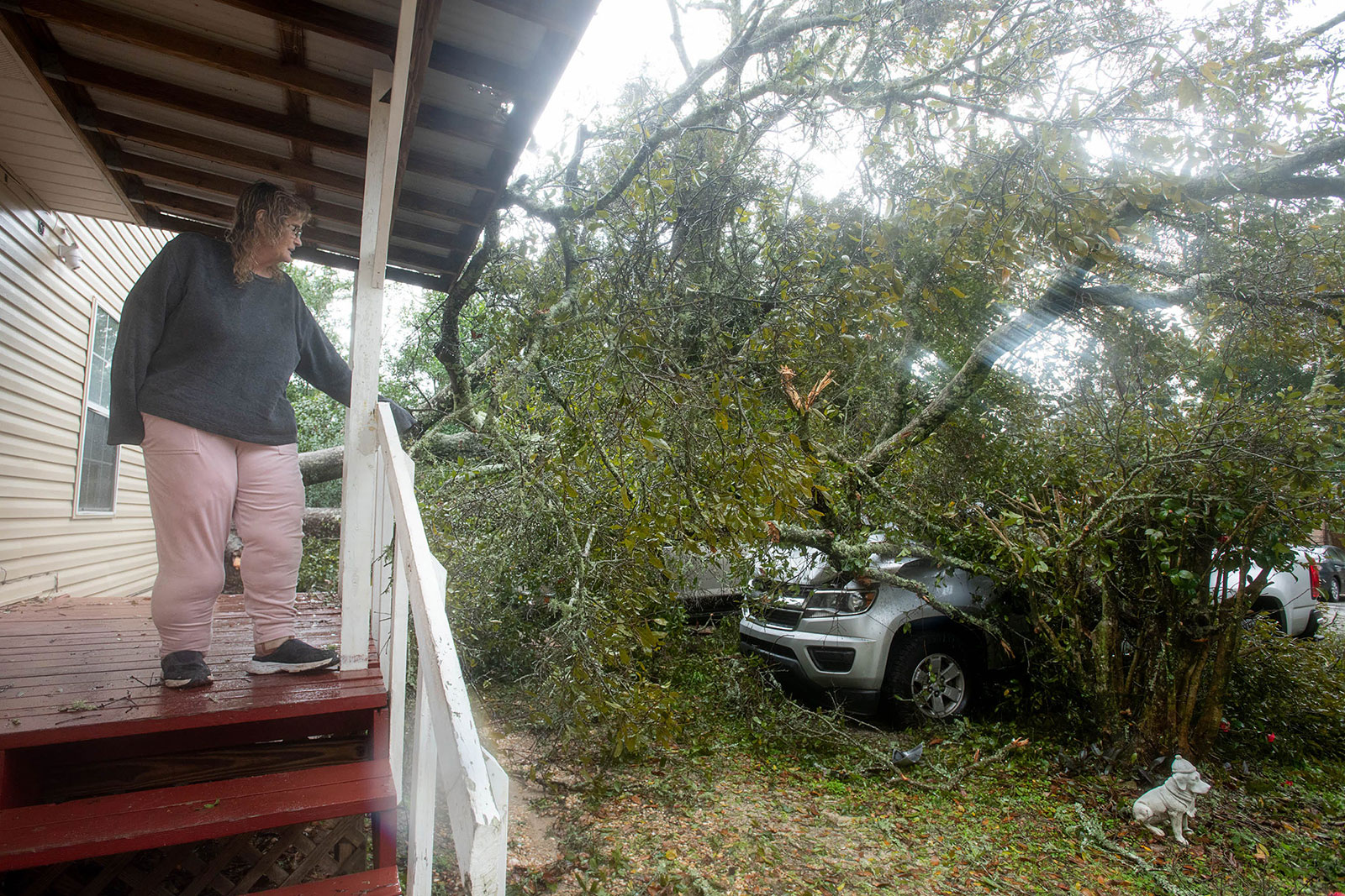 Linda Cox looks at her two vehicles that were damaged by a fallen tree in Myrtle Grove, Florida, on Tuesday.