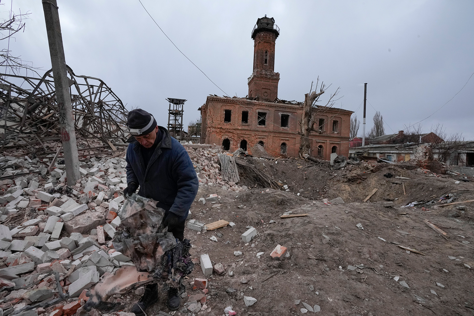 A man holds fragments of a rocket launched by the Russian forces at night, a rocket crater behind him, in the center of Kharkiv, Ukraine, on Sunday, March 27.