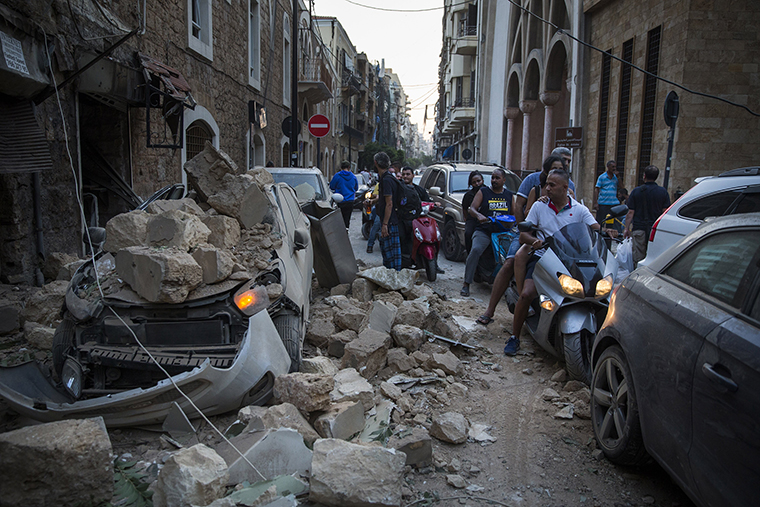 People ride past a car destroyed after a building wall collapsed on August 4.