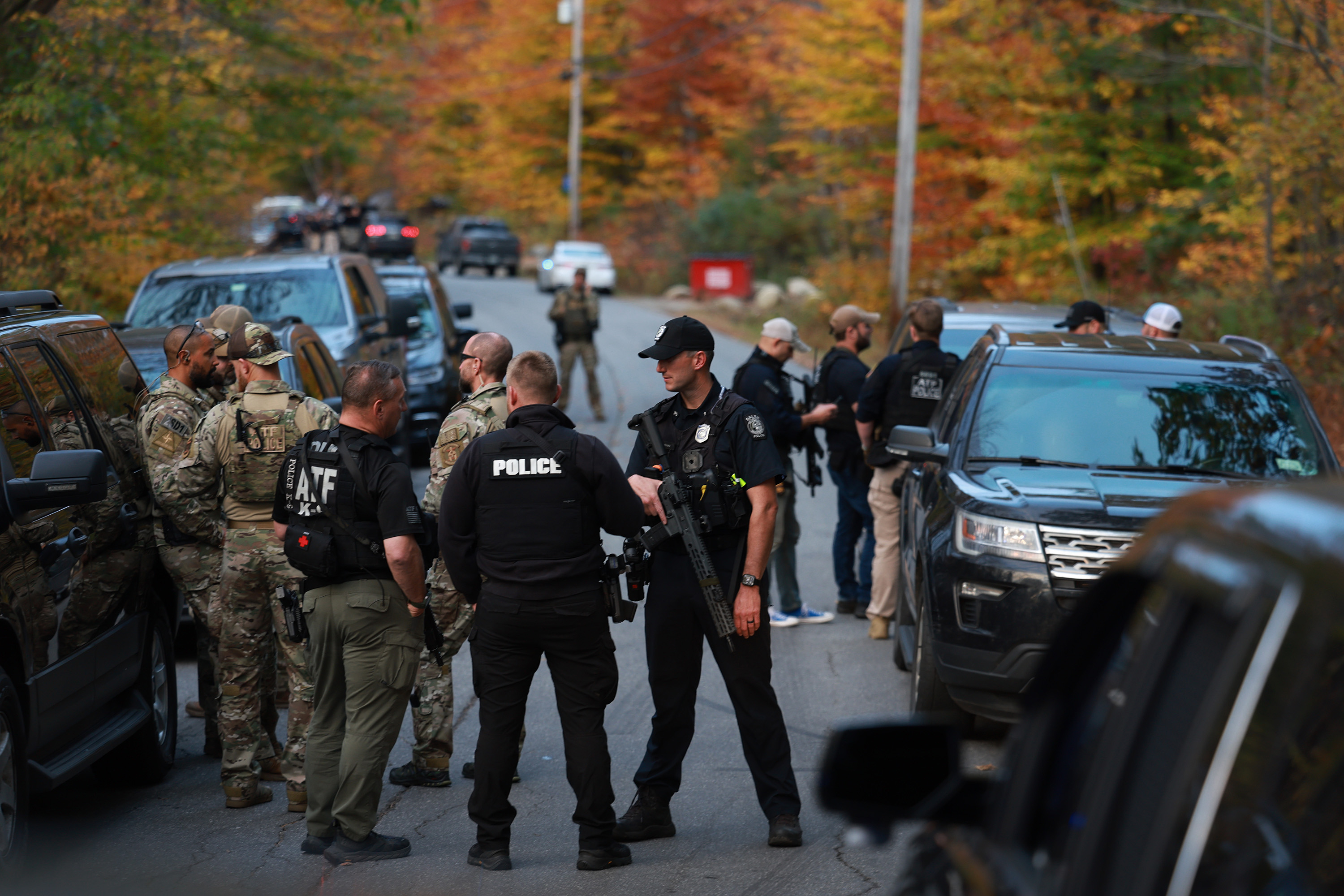 Law enforcement officials gather in the road leading to the home of the suspect being sought in connection with two mass shootings on October 26, in Bowdoin, Maine.