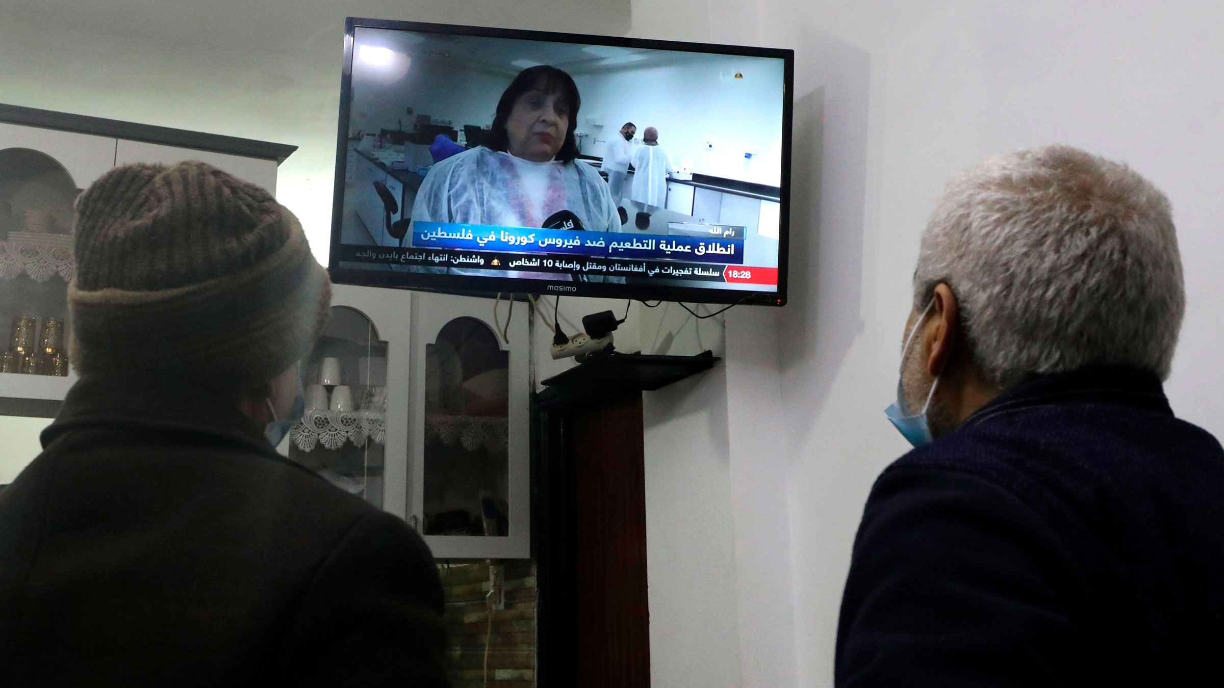 Men in Hebron, West Bank, watch a live television broadcast as Palestinian Health Minister Mai Al-Kaila announces the start of Covid-19 vaccinations.