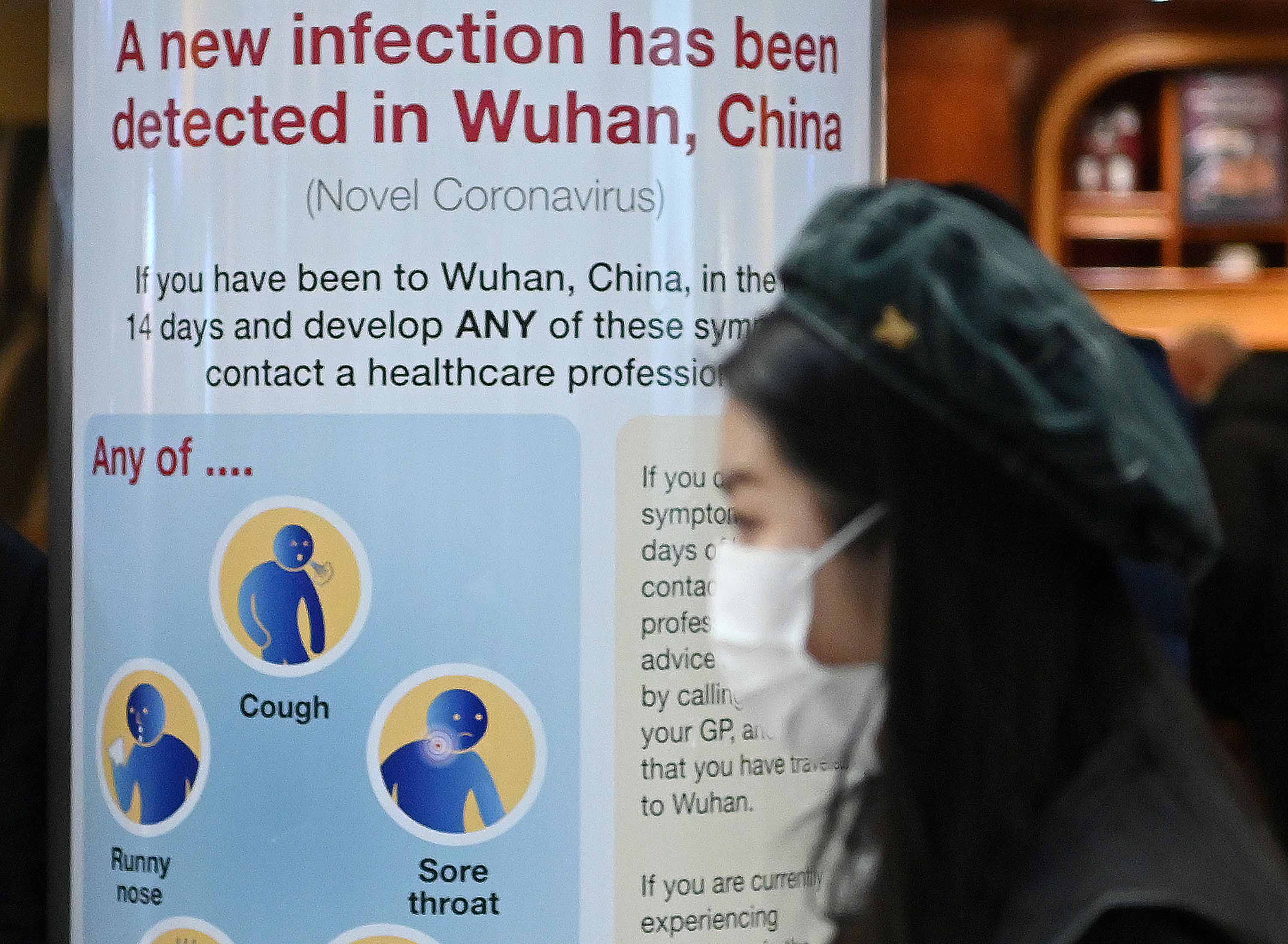 A woman wearing a face mask passes a Public Health England sign, warning passengers about the Coronavirus at Terminal 4 of London Heathrow Airport on Tuesday.