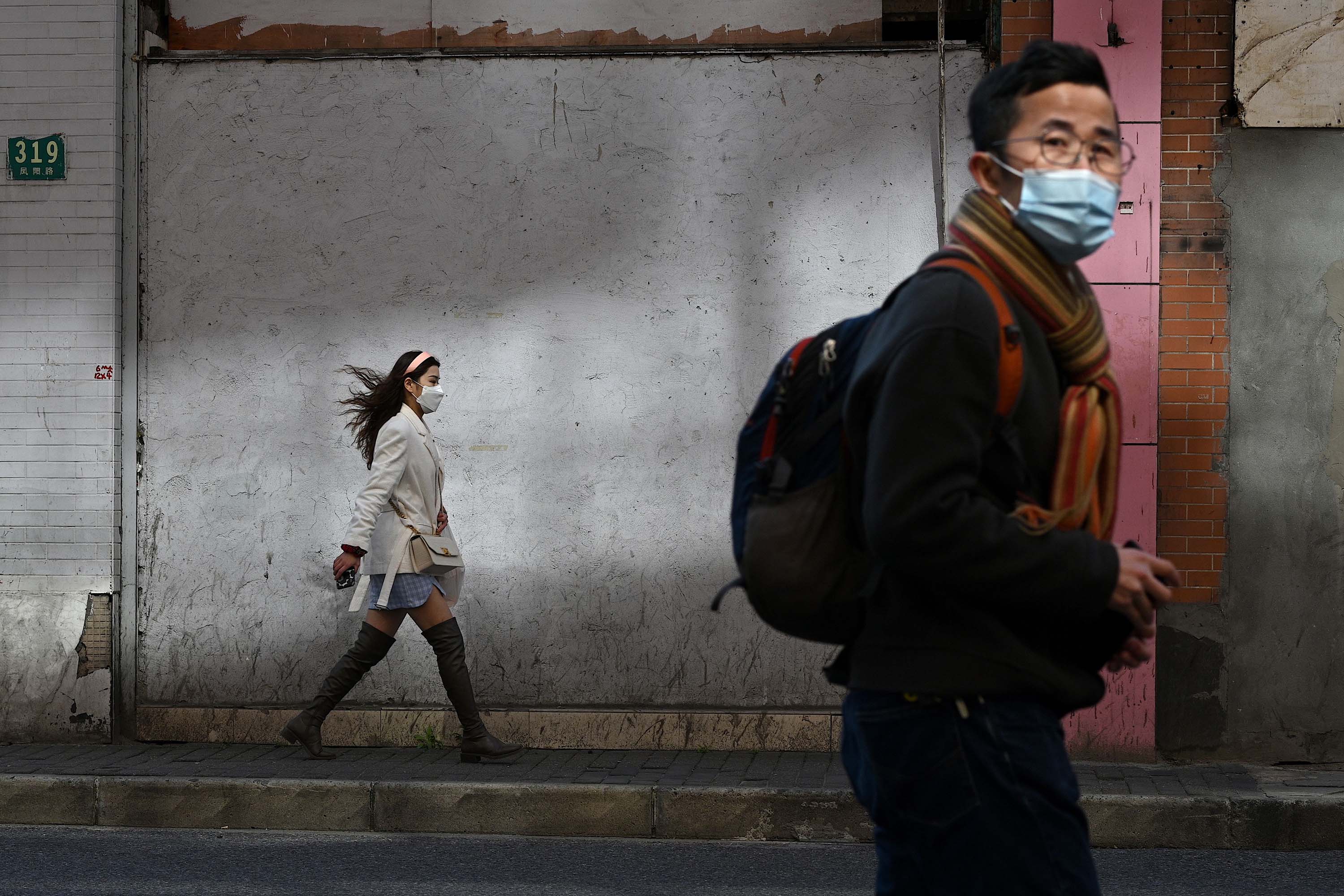 Pedestrians wearing protective face masks walk along a street in Shanghai on Monday.