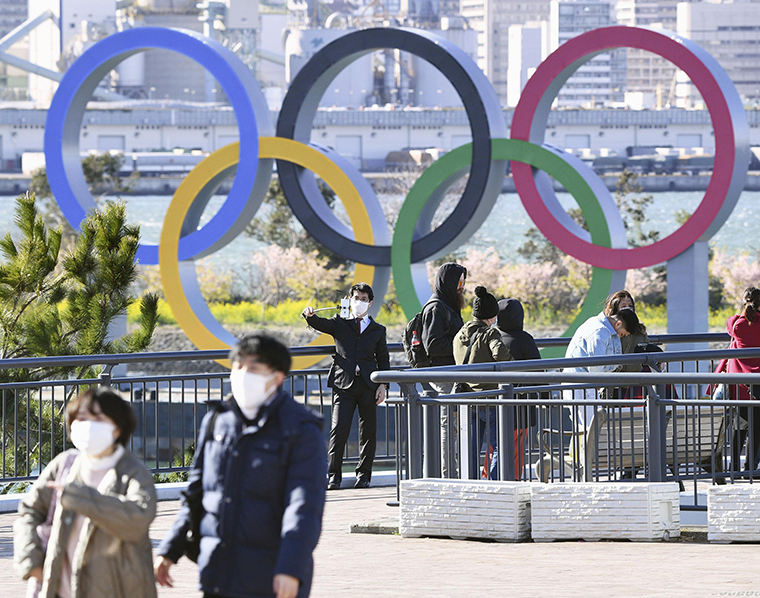 People wear masks near the Olympics rings in Tokyo's Daiba waterfront area on Thursday, March 5. 