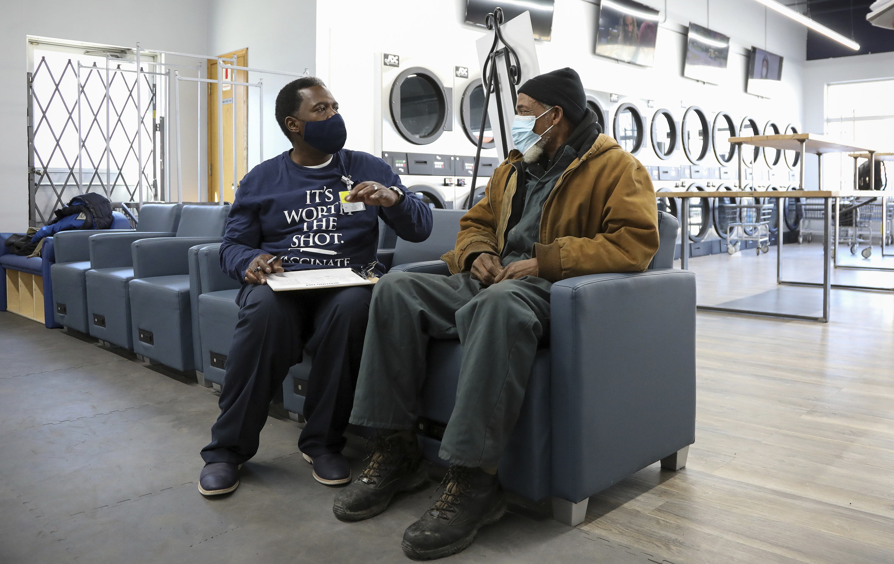 Community outreach worker Herman Simmons, left, makes a vaccination appointment for Theopulis Polk, right, at a Chicago laundromat on Saturday, March 6.