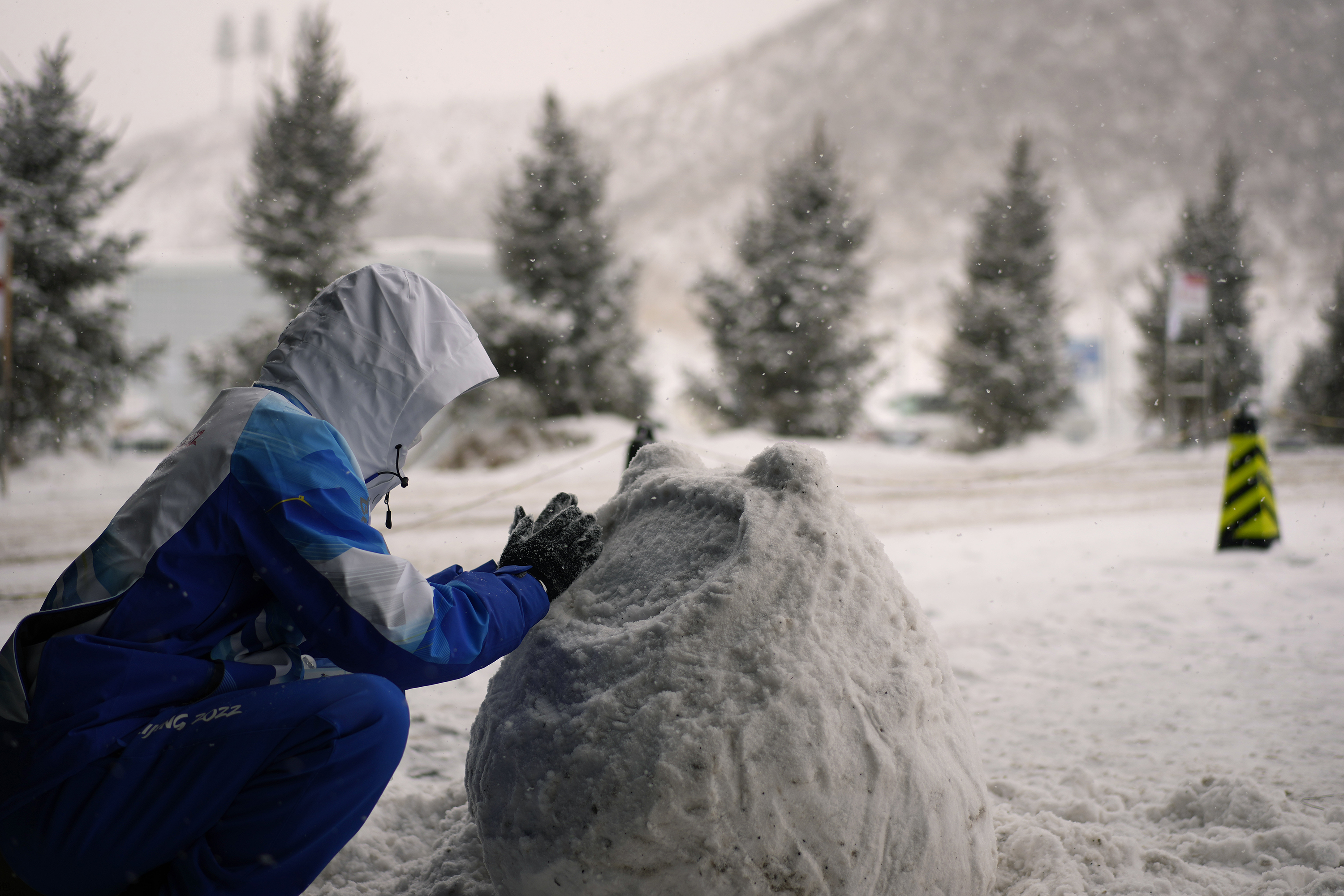 A volunteer sculpts Olympic mascot Bing Dwen Dwen from snow during a snowstorm on Sunday.
