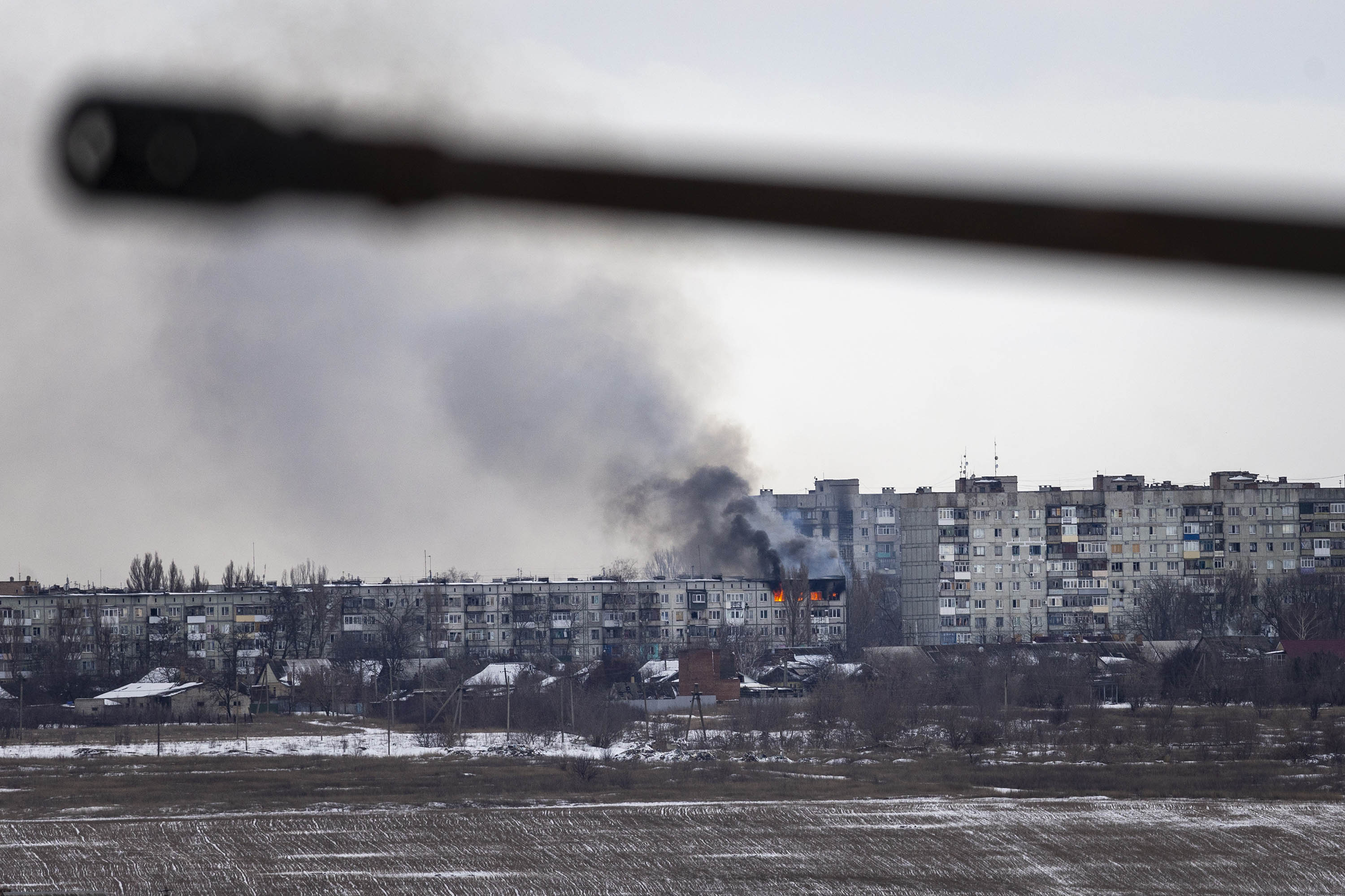 A Ukrainian military vehicle drives by as an apartment building hit by Russian artillery burns in the distance on February 14, in Bakhmut, Ukraine.