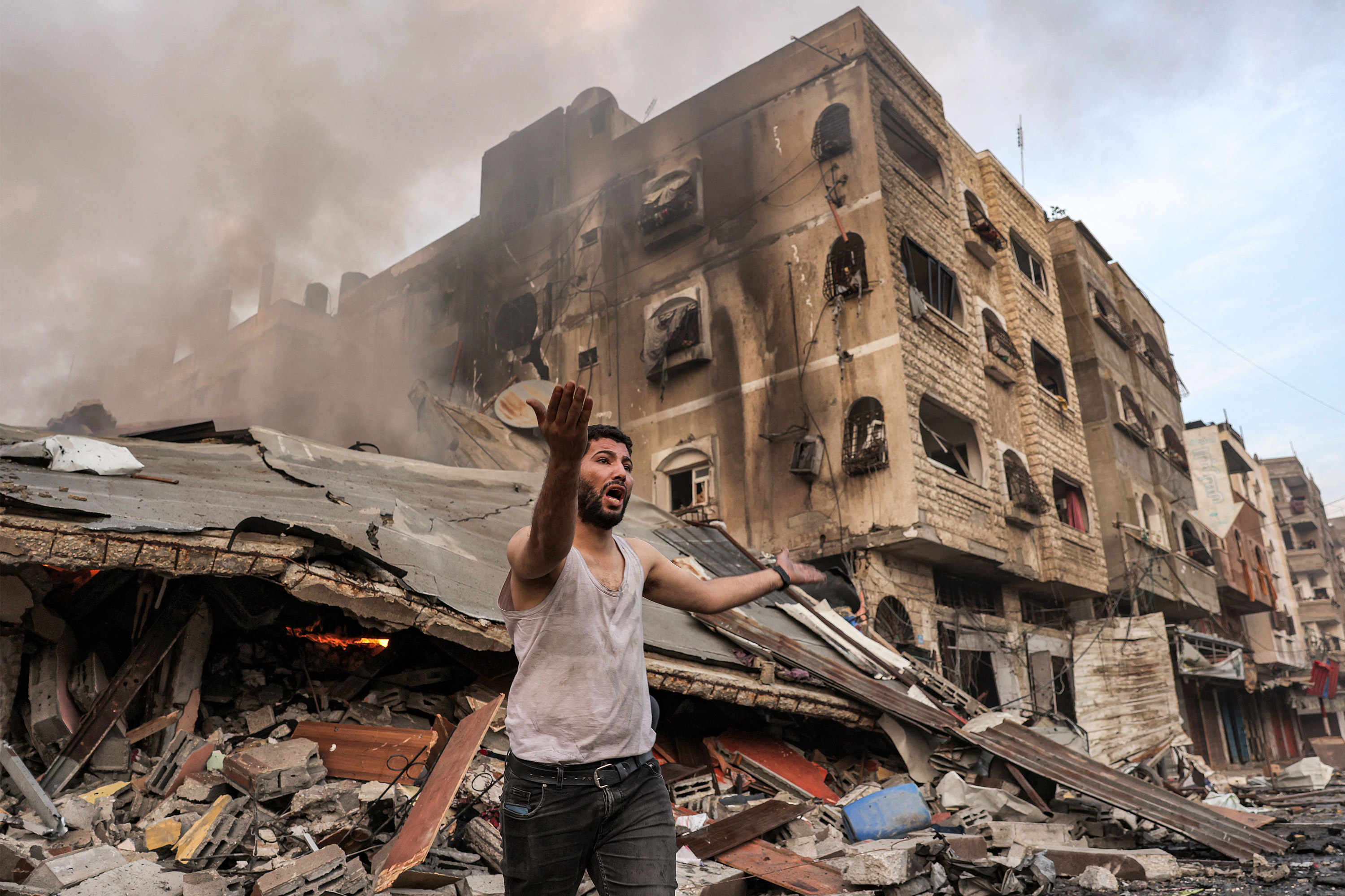 A man reacts outside of a burning collapsed building, following Israeli bombardment, in Gaza City on October 11, 2023.