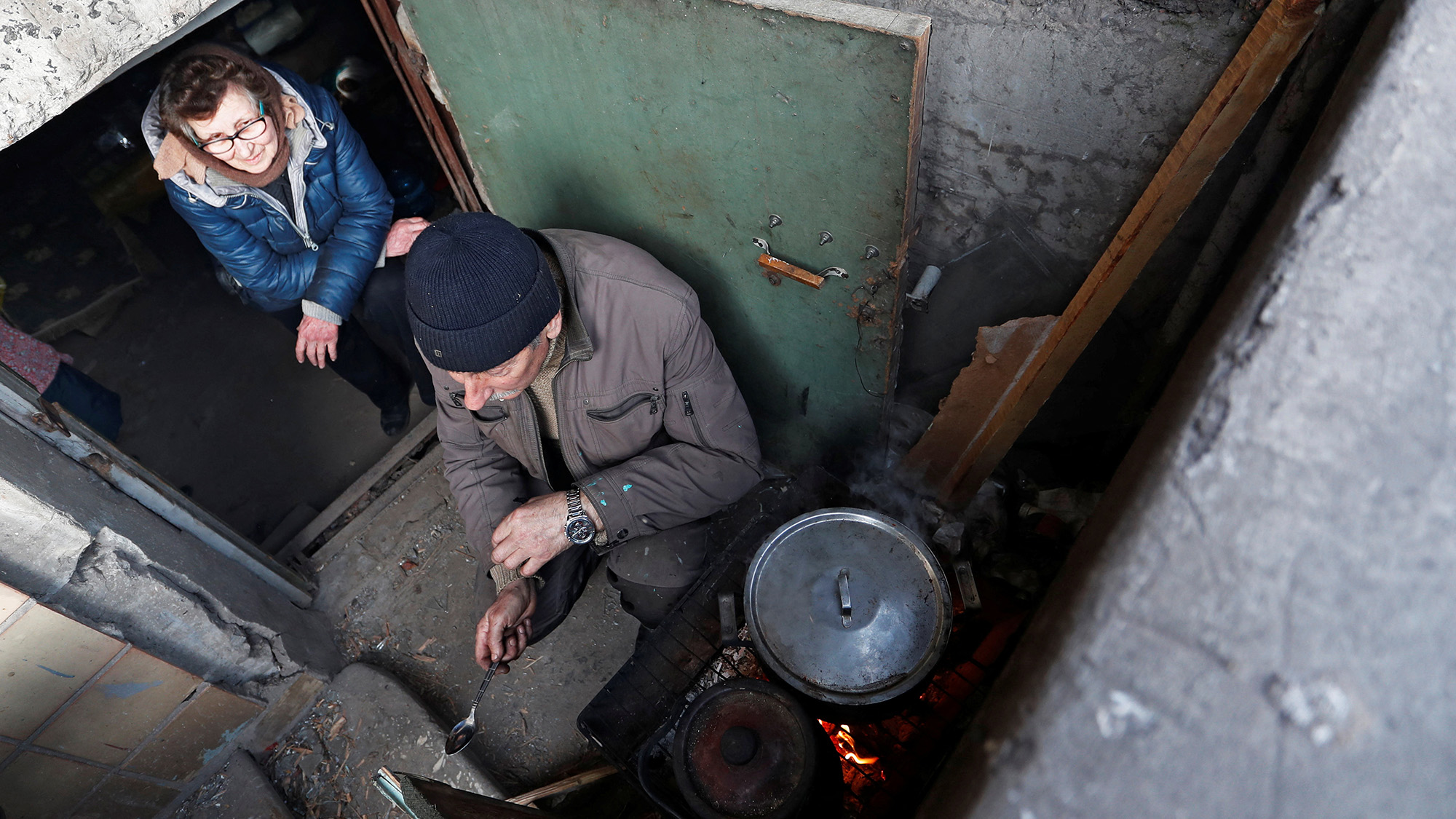 Lyudmila, 71, and Viktor, 63, cook food at the entrance to the basement of an apartment building in the besieged city of Mariupol, Ukraine on March 30.