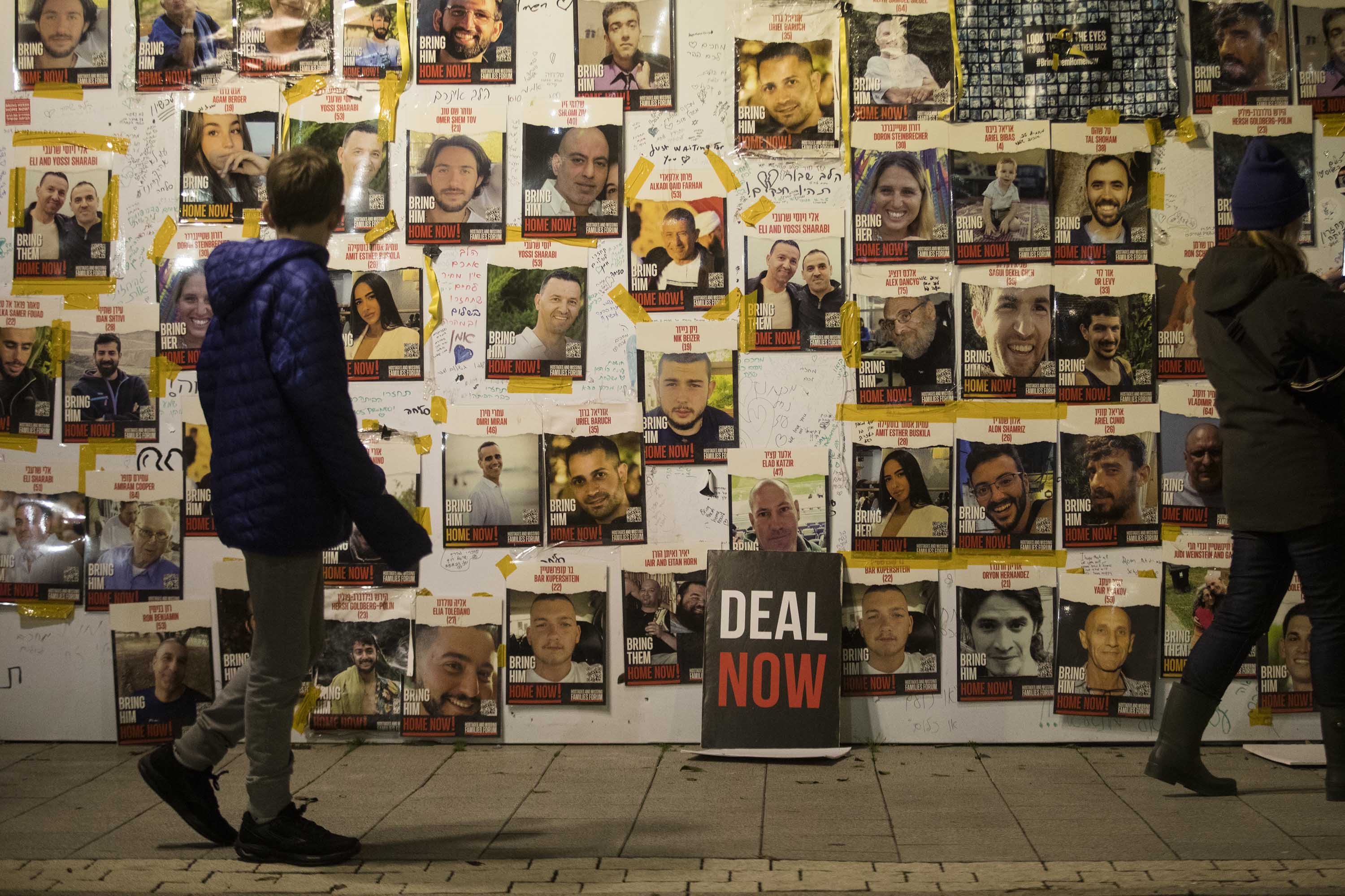 People walk by a wall with photos of hostages held by Hamas in Gaza, during a rally calling for release of all hostages, on January 27, in Tel Aviv, Israel. 