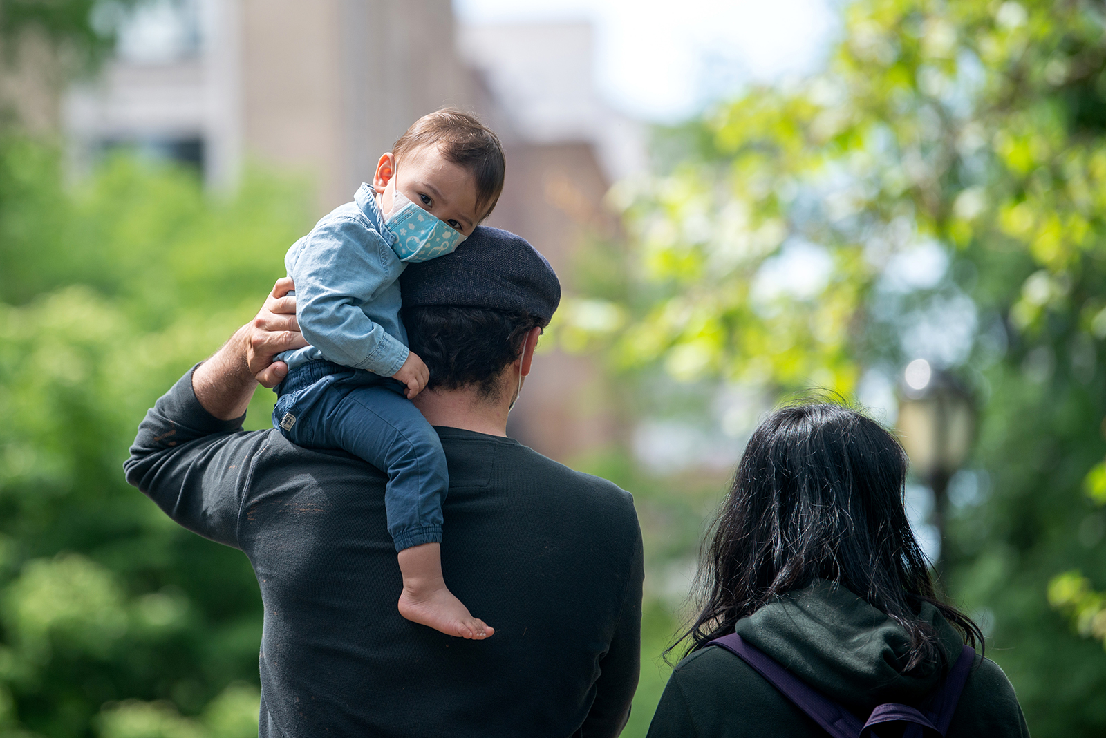 A youngster wearing a mask looks at the camera while sitting on his father's shoulder in Central Park in New York, on May 24.