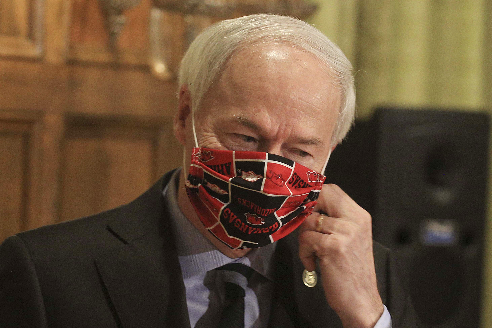 In this April 27, 2020 file photo, Gov. Asa Hutchinson takes off his Arkansas Razorbacks facemark as he arrives for the daily coronavirus briefing at the state Capitol in Little Rock. 