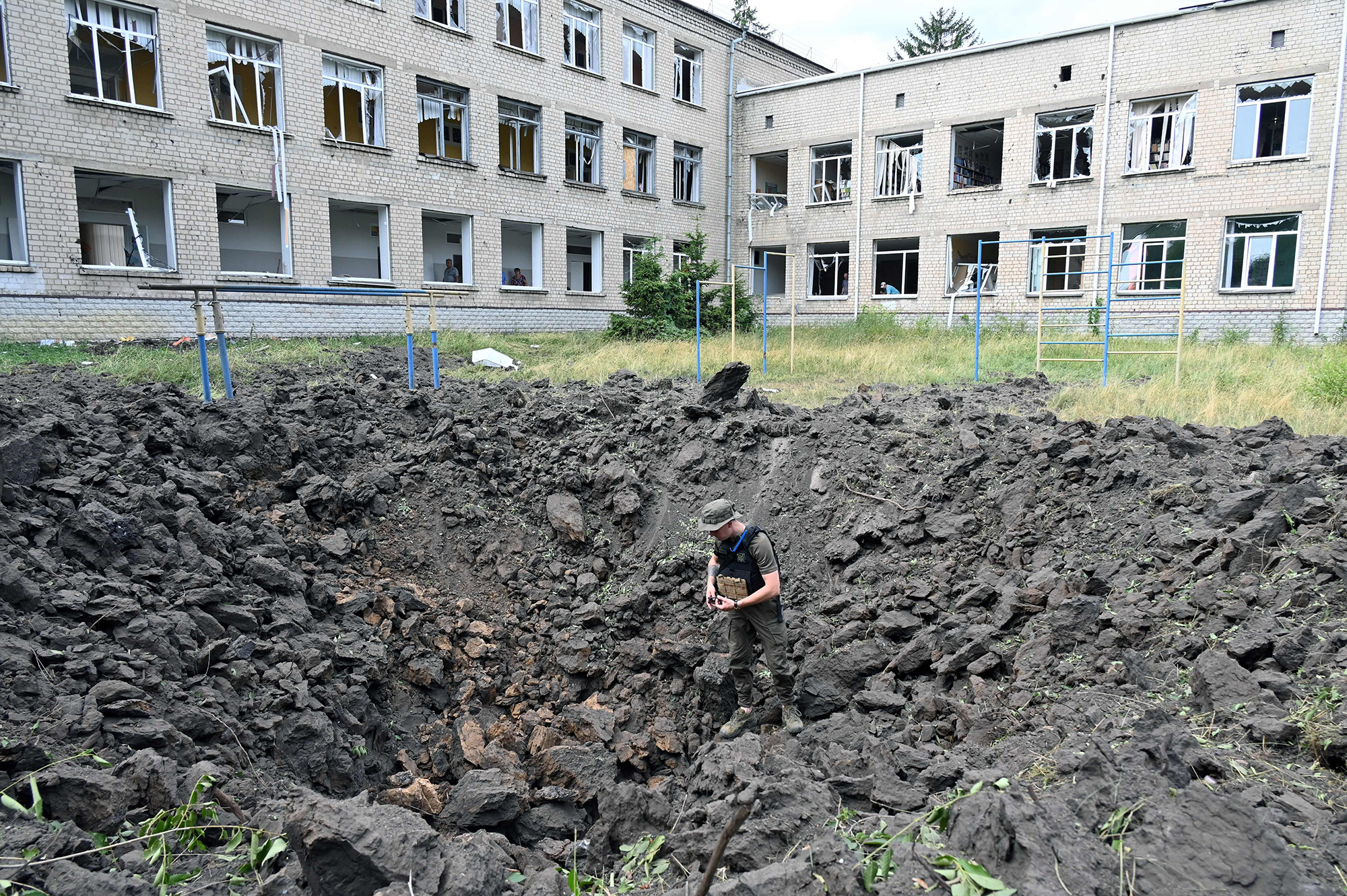 An Ukrainian serviceman examines a crater outside a school in Kharkiv, Ukraine, on July 7.
