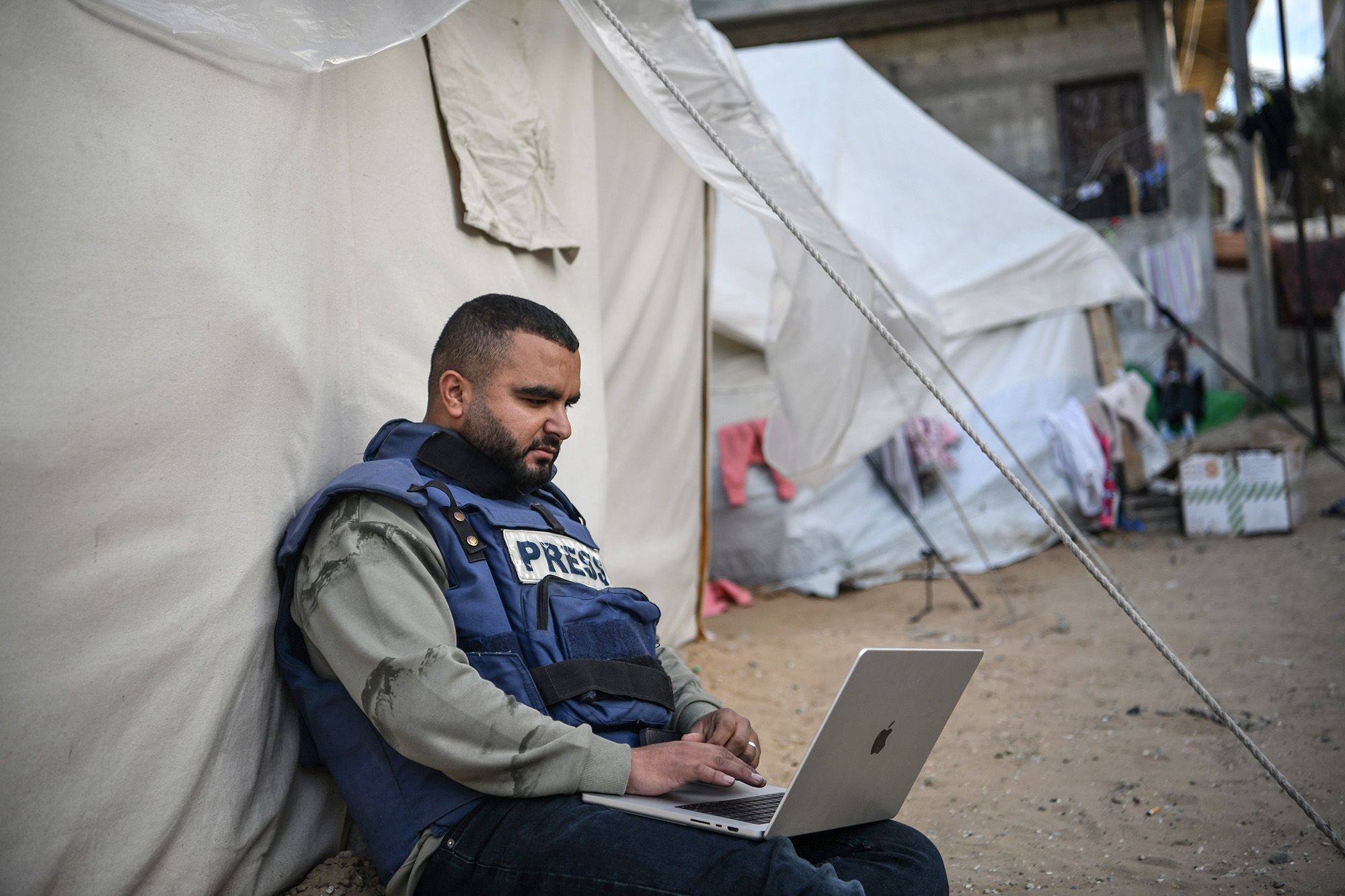 A press member is seen sitting next to a tent as he tries to connect to the internet in Rafah, Gaza, on January 14.