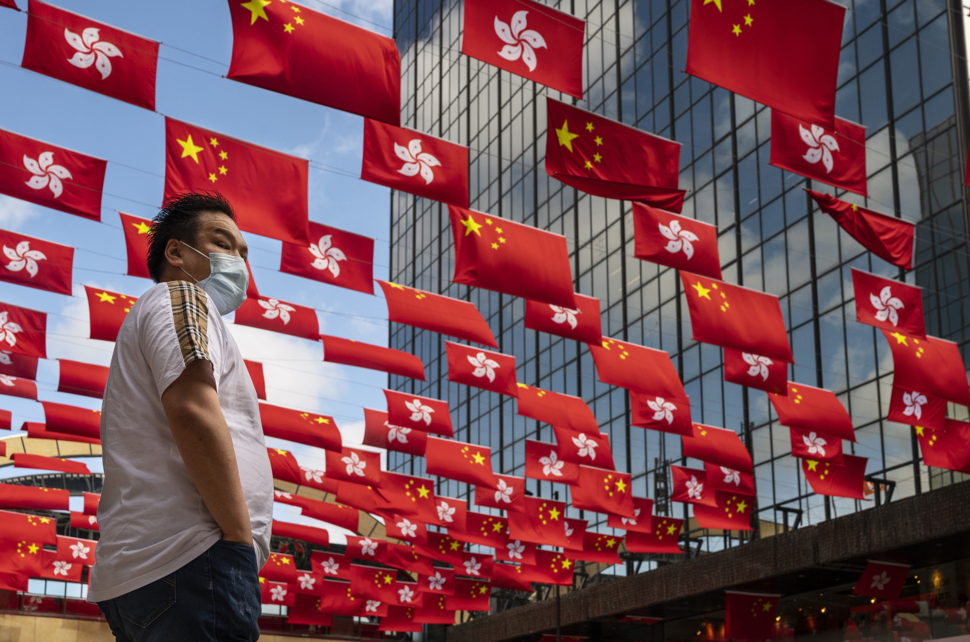 27 Haziran'da Hong Kong'da 1 Temmuz yıldönümü öncesinde Çin ve Hong Kong bayrakları sergilenirken bir yaya karşıdan karşıya geçmek için bekliyor. 