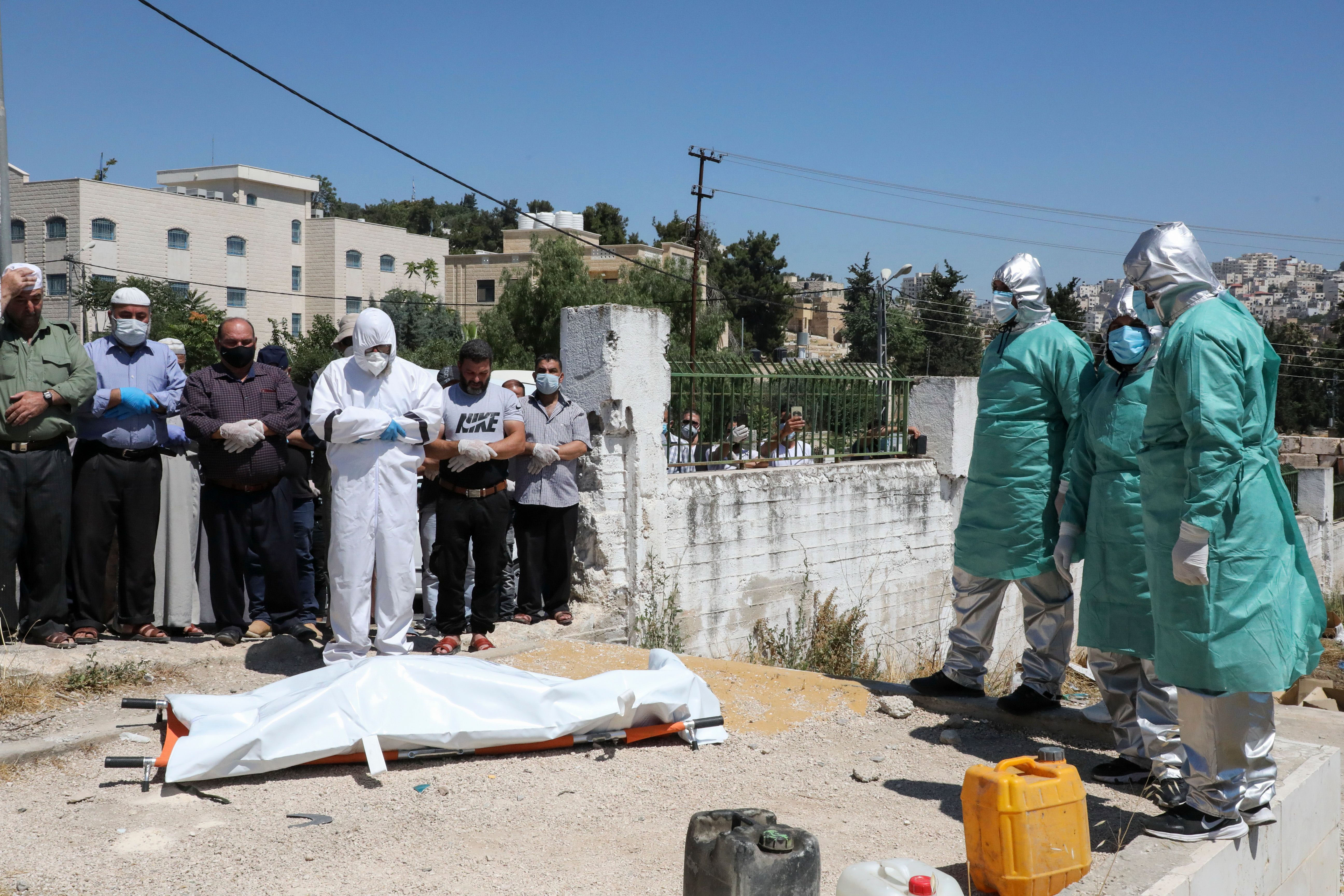 Relatives and staff from the Palestinian Ministry of Health stand by the body of a person said to have died from Covid-19 before burial in the southern West Bank city of Hebron on June 29.