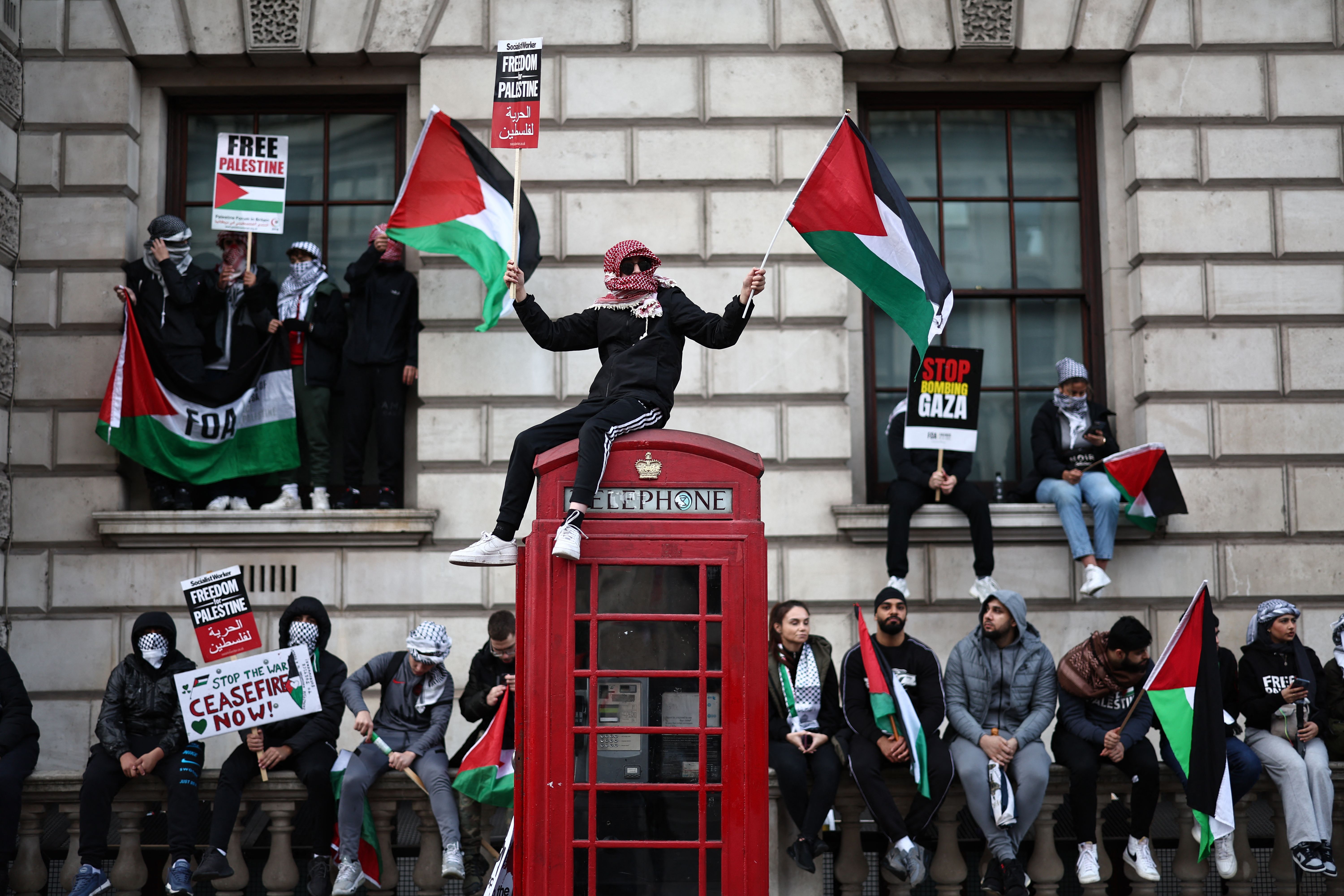 A protester waves Palestinian flags sitting on a red telephone box on Whitehall during the 'March For Palestine' in London, on October 28, to call for a ceasefire in the conflict between Israel and Hamas.