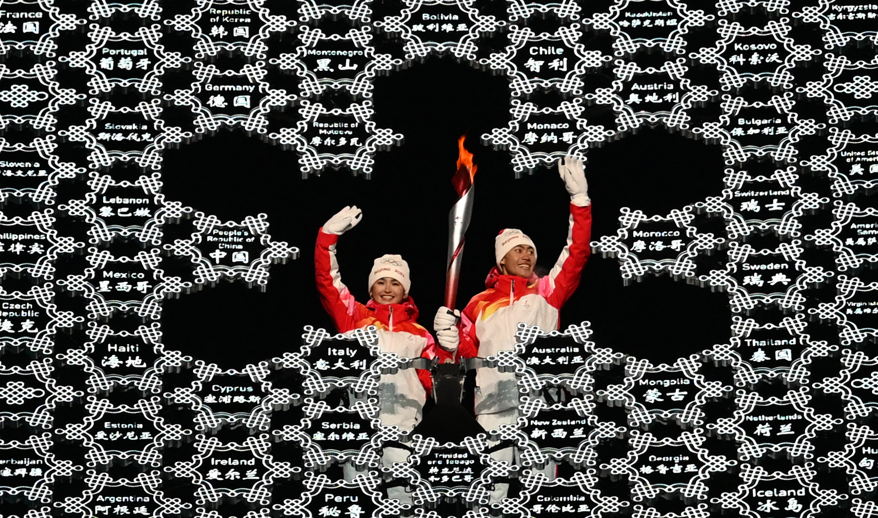 Chinese torchbearers Dinigeer Yilamujian (L) and Zhao Jiawen wave with the Olympic flame in the middle of a giant snowflake during the Opening Ceremony of the Beijing 2022 Winter Olympic Games.