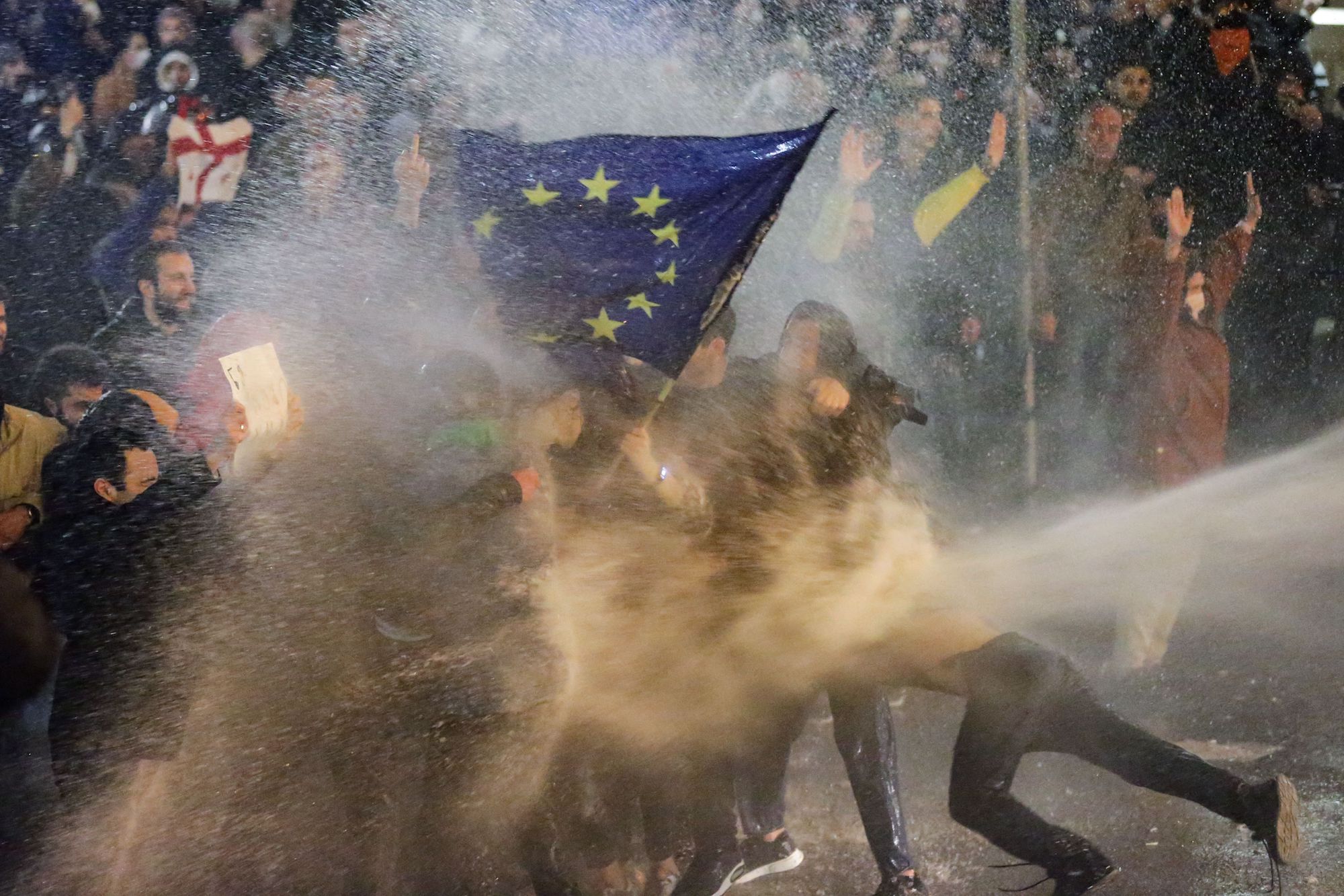 I manifestanti che sventolano una bandiera dell'Unione europea vengono spruzzati da un cannone ad acqua durante gli scontri con la polizia antisommossa vicino al parlamento georgiano.