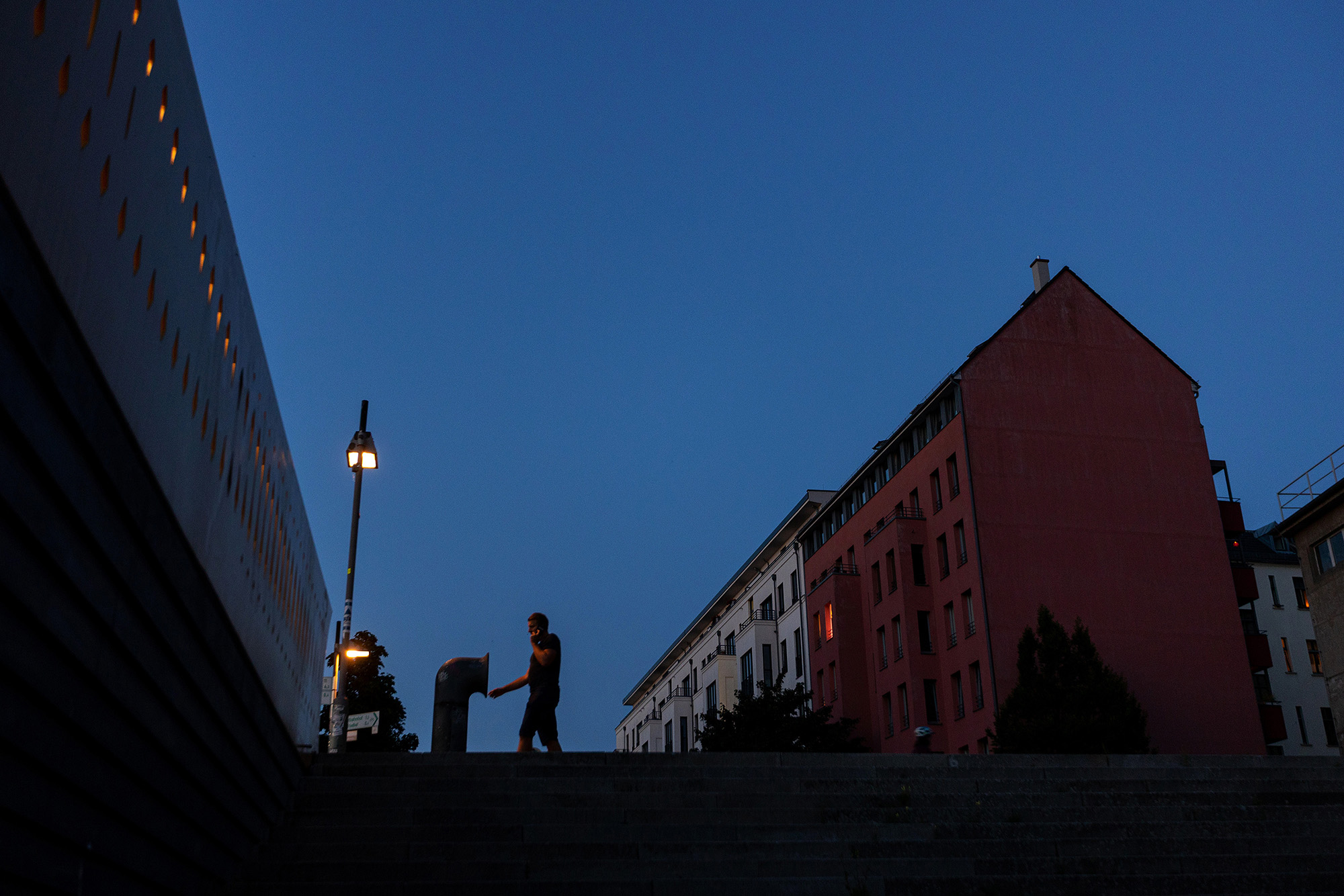 A street lamp illuminates a resident outside part of an apartment complex lit up at sunset in Berlin on Tuesday, August 16.