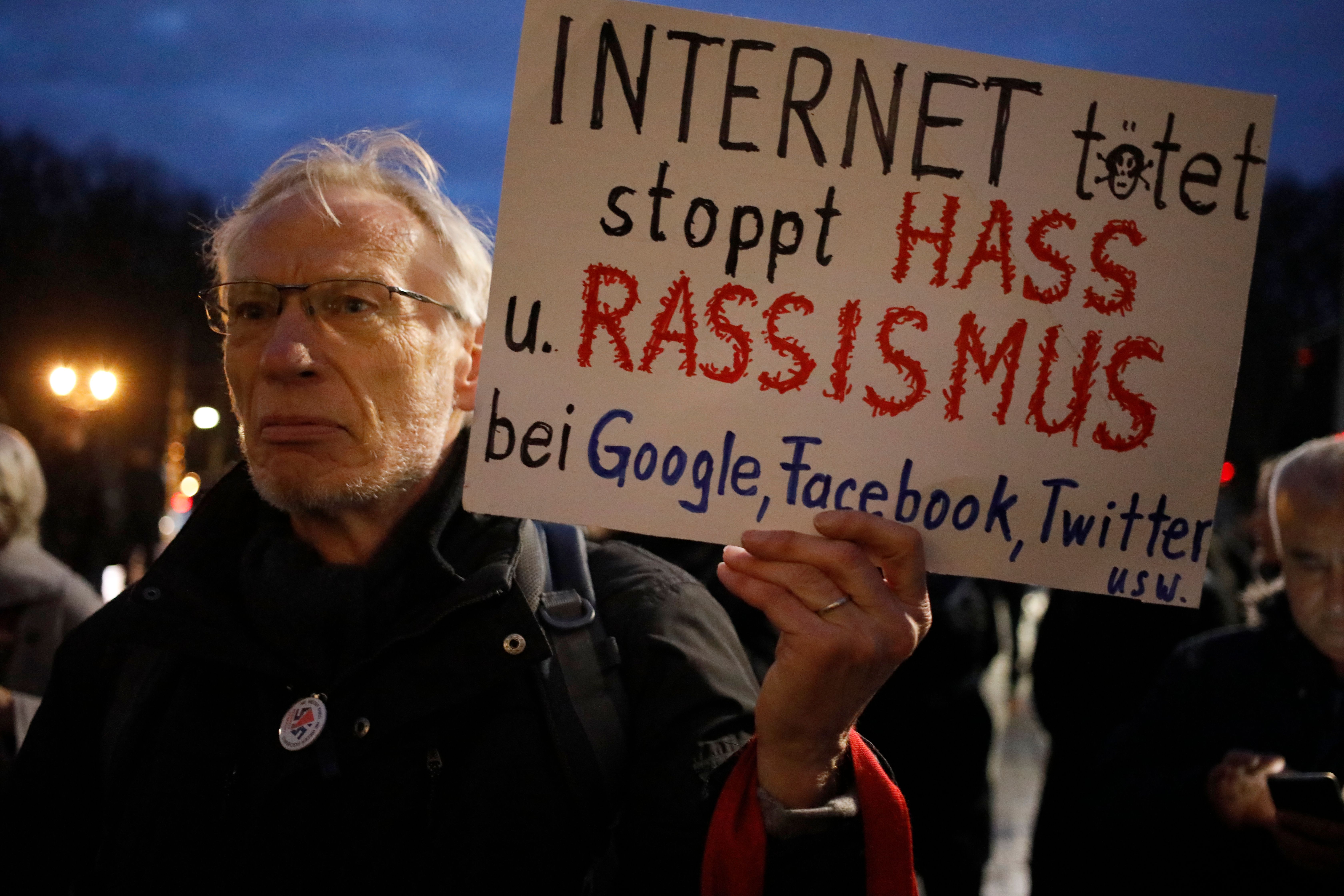 A man holds a poster reading "Internet kills - stop hate and racism at Google, Facebook, Twitter etc" during a vigil in solidarity with the Hanau shooting victims and their families, in front of Brandenburg Gate in Berlin on Thursday, February 20, a day after at least nine people were killed in two shootings.