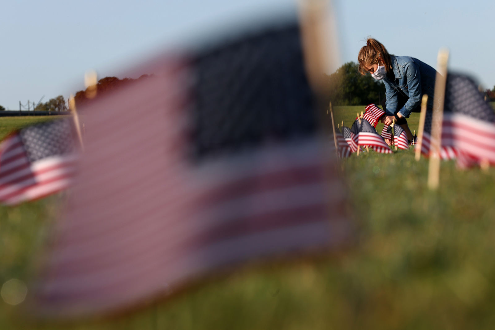 A woman places flags at a COVID Memorial Project installation of 20,000 American flags on the National Mall in Washington, DC, on September 22. The flags are displayed on the grounds of the Washington Monument facing the White House. 