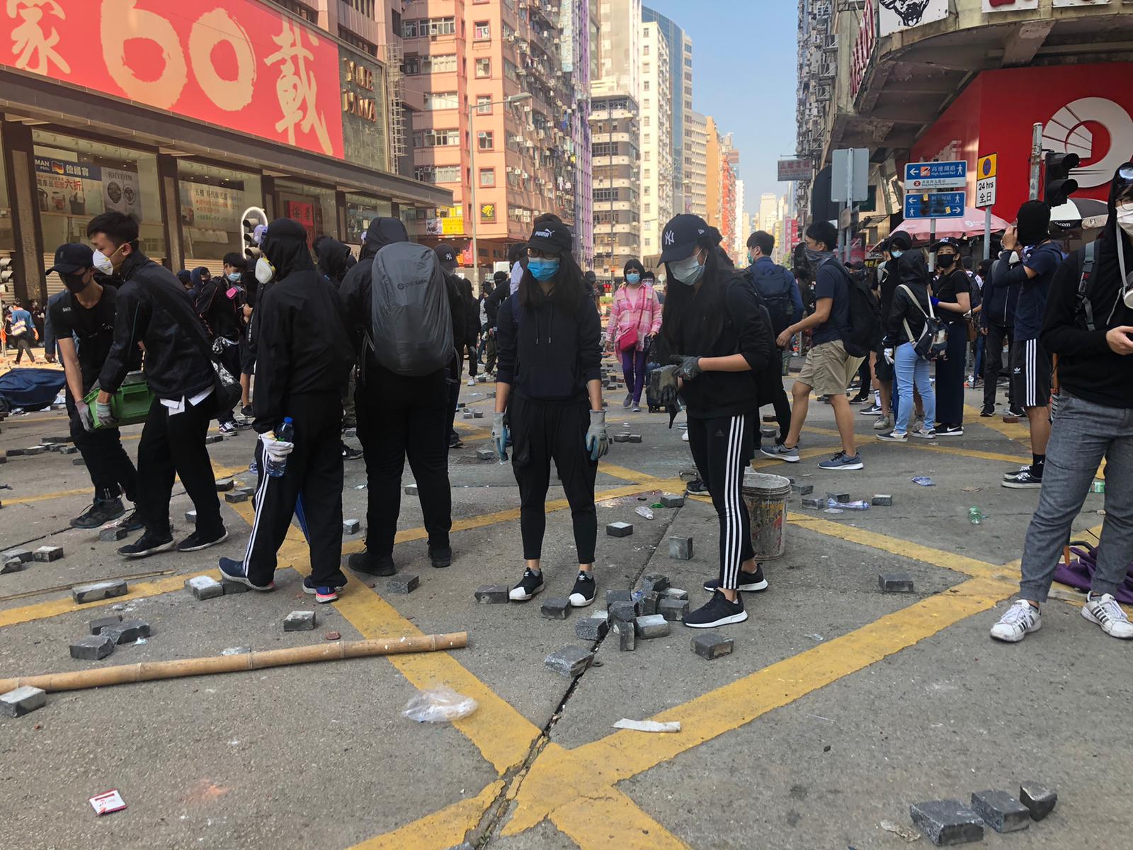 Protesters in Kowloon, Hong Kong, are throwing bricks and makeshift barricades onto the roads.