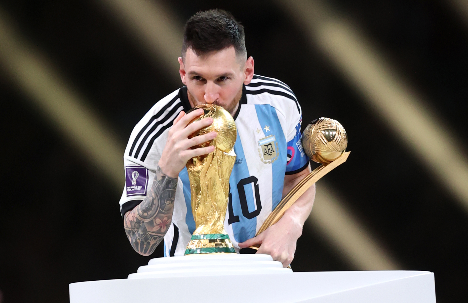 Messi, holding the Golden Ball trophy, kisses the World Cup.