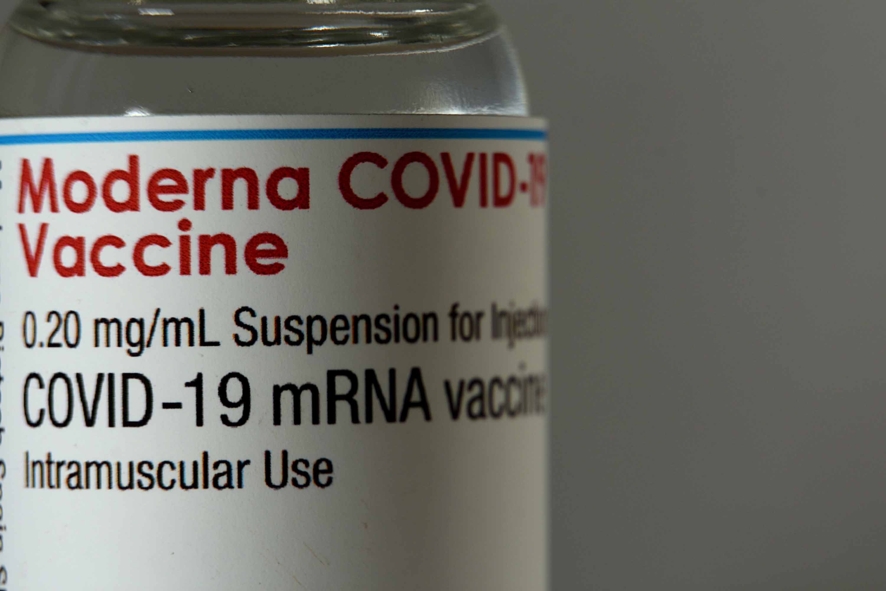 A close-up shows a vial of the Moderna vaccine.