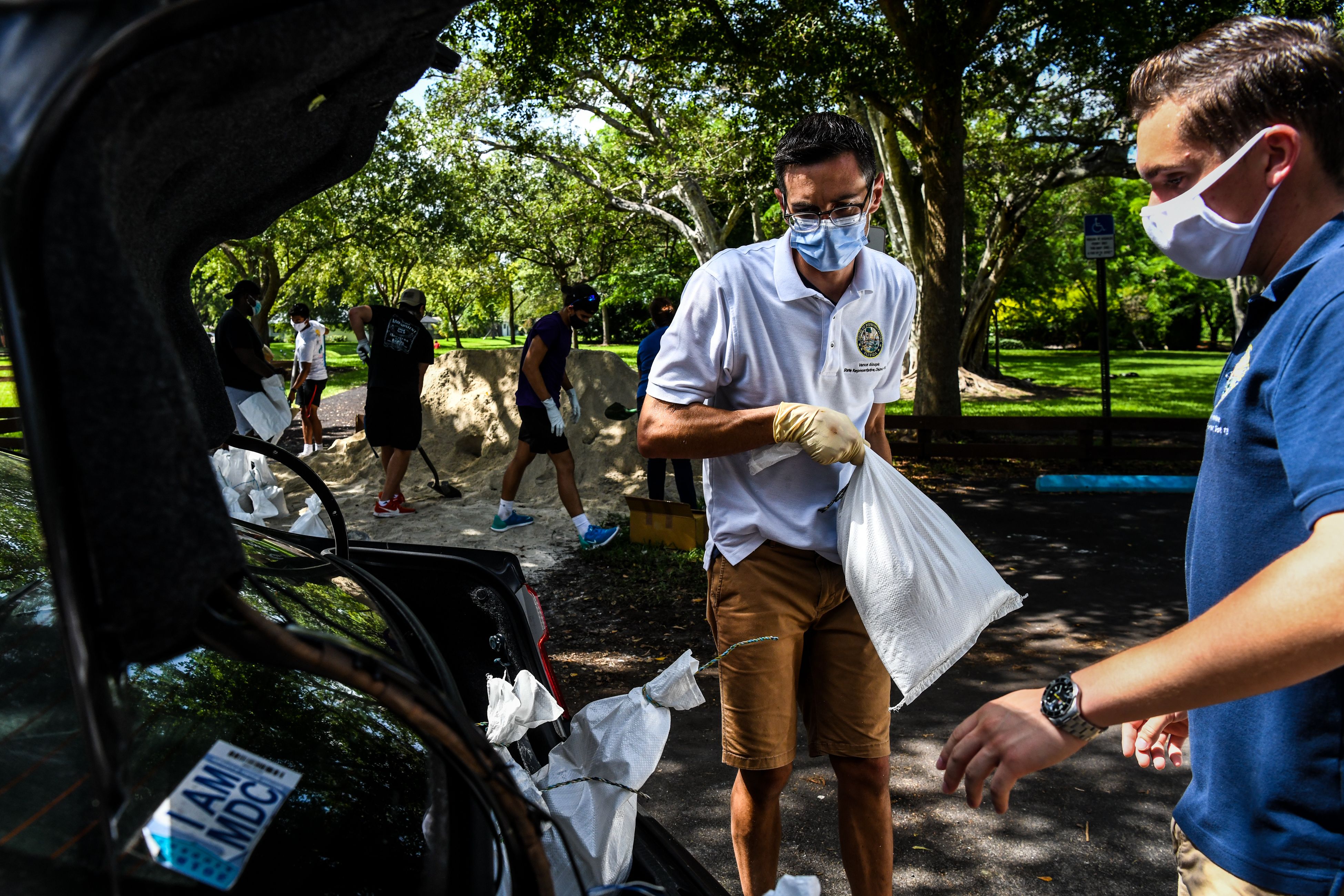 Member of Florida House of Representatives Vance Aloupis (center) puts sand bags in a resident's car trunk in Palmetto Bay near Miami, on Friday as Floridians prepare for Hurricane Isaias.