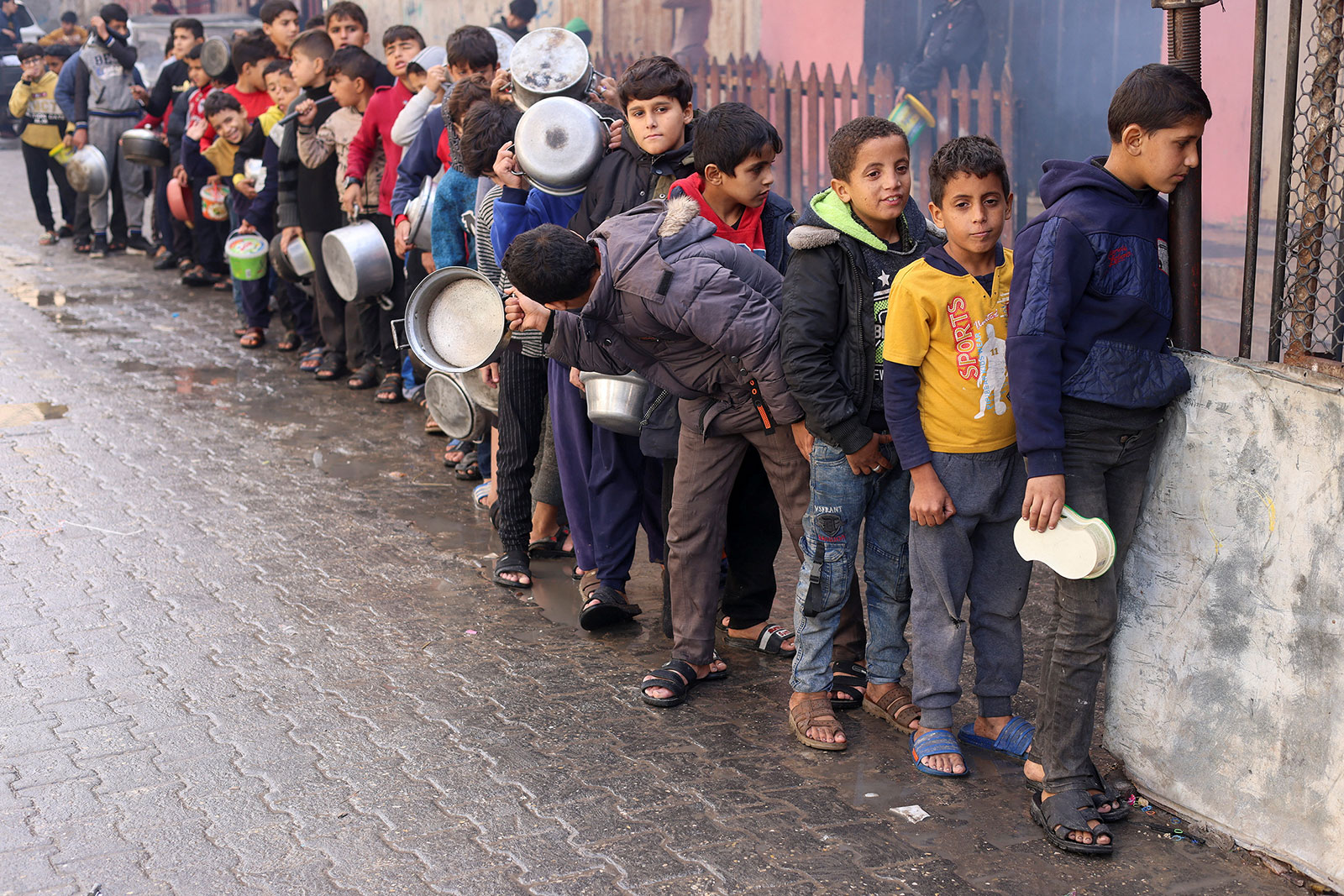 Palestinian children carry pots as they wait to receive food cooked by a charity kitchen, in Rafah, Gaza, on December 14.