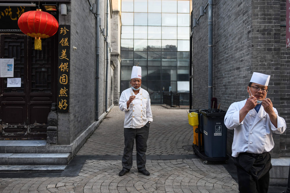 A chef lowers his face mask, worn as a preventive measure against the coronavirus, while he smokes a cigarette outside a restaurant in a quiet tourist area in Beijing on April 2. 