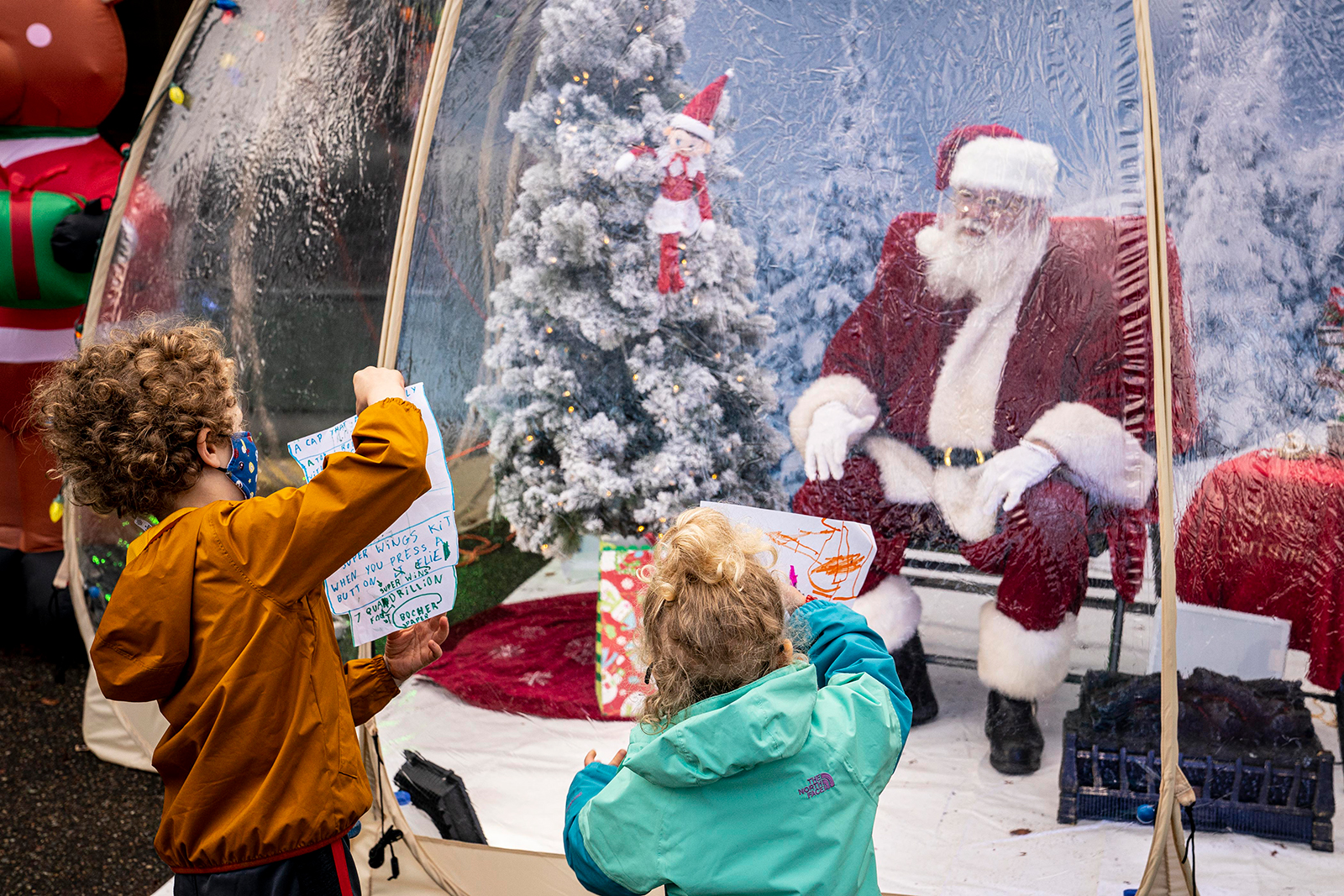 (From left) Mateo Johnson, 6, and Neah Johnson, 3, visit with Santa, who holds court in a snow globe December 6 in Seattle. Covid-19 safety measures have opened the door for rethinking how kids physically interact with Santa.