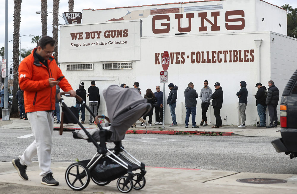A man walks with a stroller as people stand in line outside the Martin B. Retting gun store on March 15, in Culver City, California.