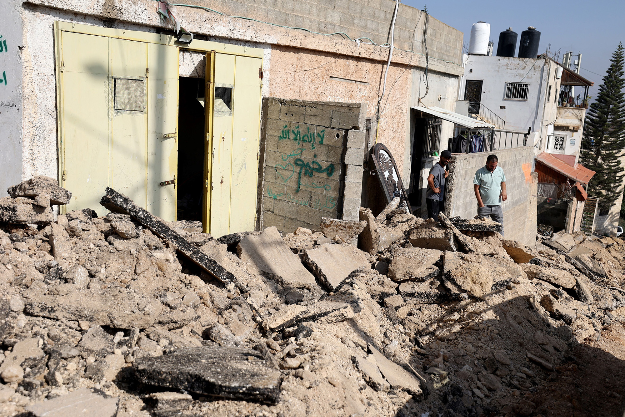 Palestinian men stand outside a building at the edges a road ripped up by an Israeli manned bulldozer during an incursion and clashes in the Jenin refugee camp, West Bank, on November 3.