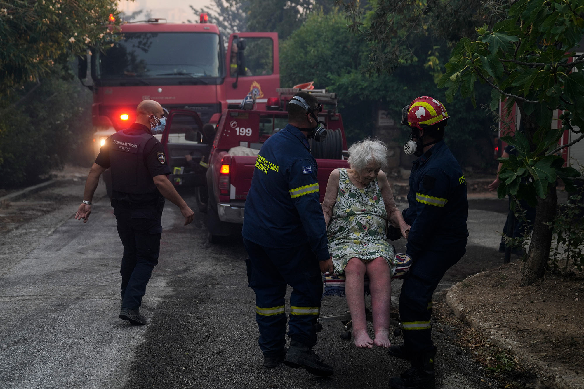 Firefighters evacuate an elderly woman from her house in Penteli, Greece, on Tuesday, July 19.