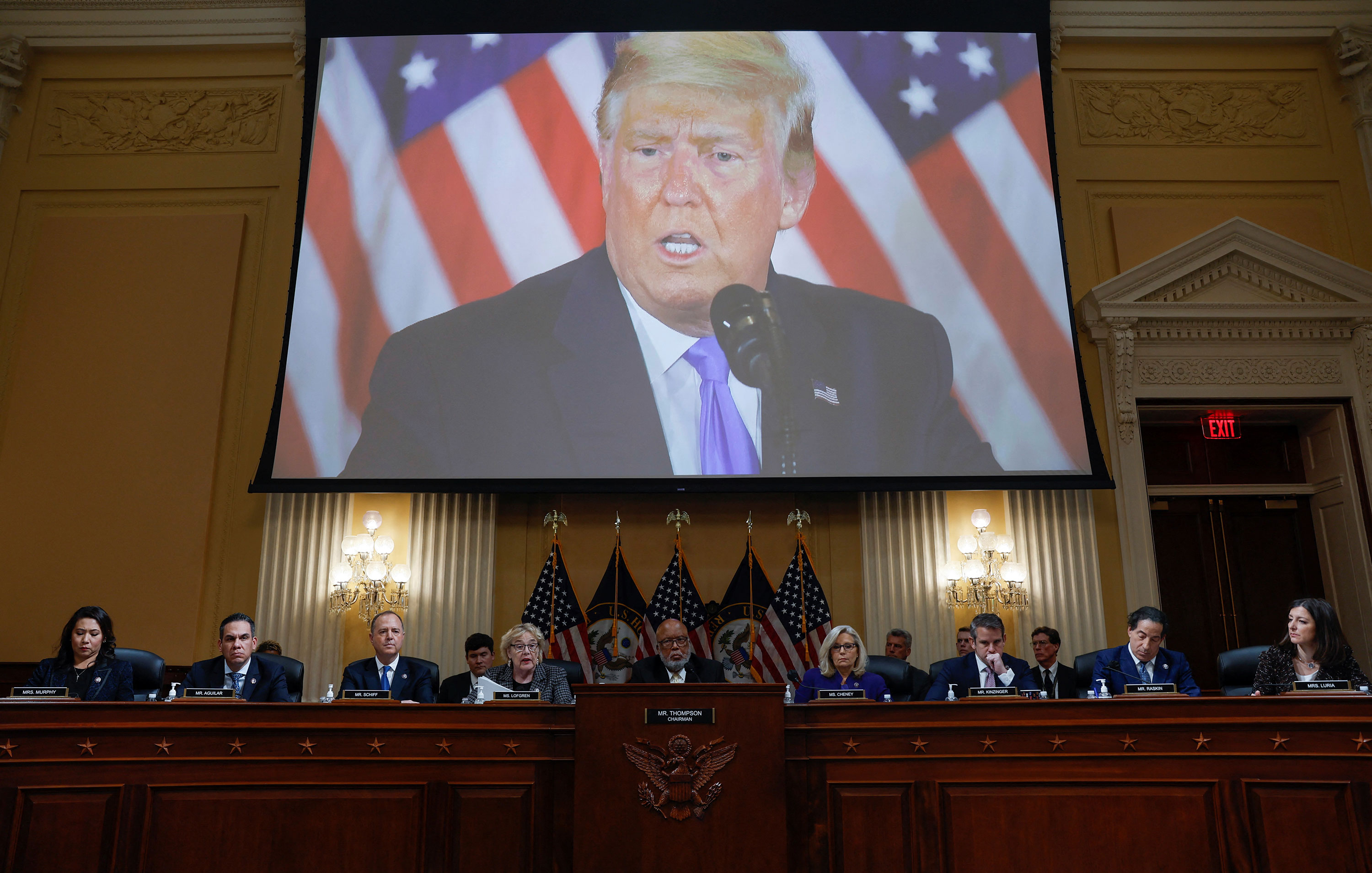 Members of the House Select Committee investigating the January 6 Attack on the U.S. Capitol sit on Monday beneath a video of former President Donald Trump talking about the results of the 2020 election.