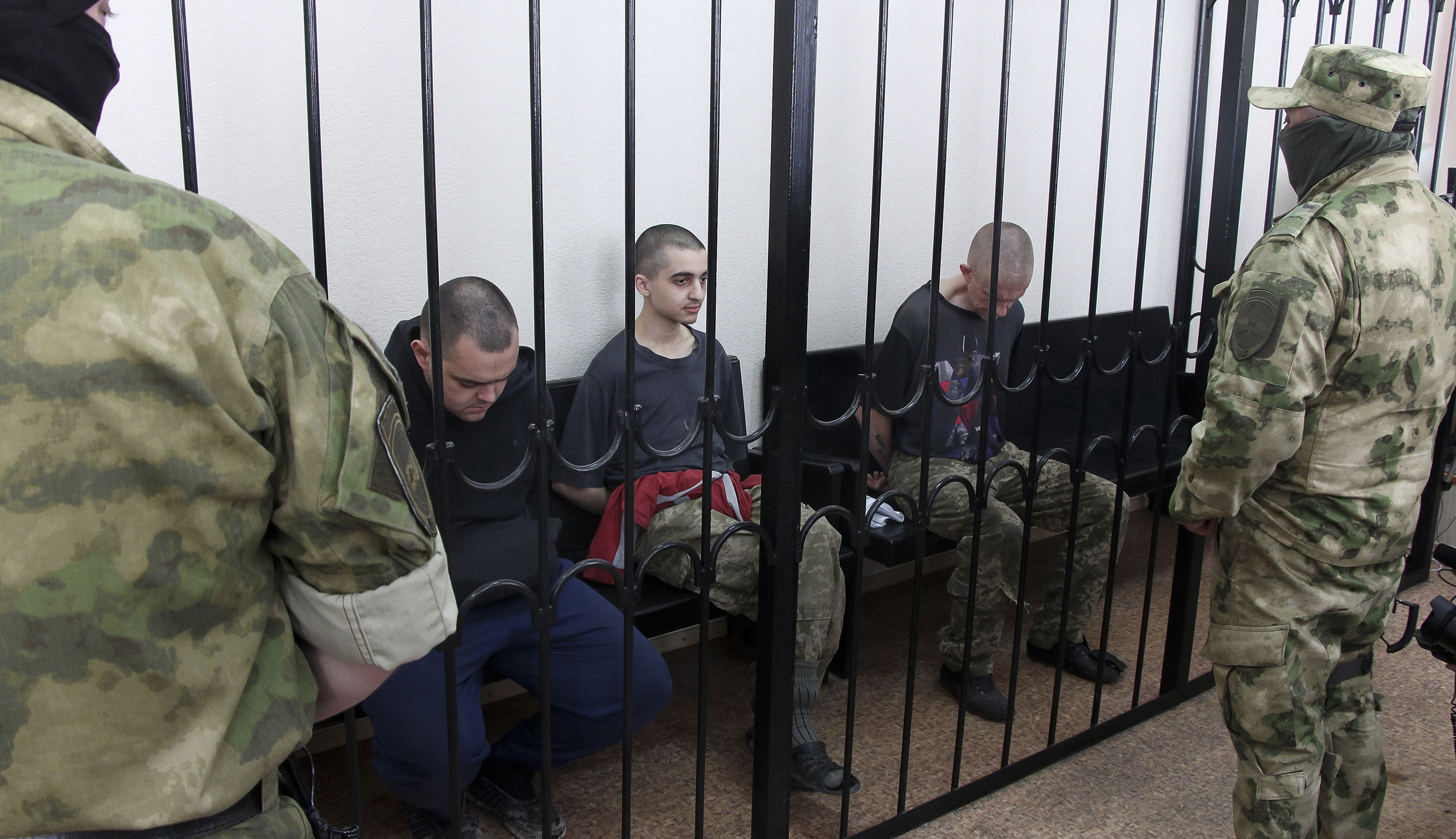 Two British citizens Aiden Aslin, left, and Shaun Pinner, right, and Moroccan Saaudun Brahim, center, sit behind bars in a courtroom in Donetsk, eastern Ukraine, on June 9.