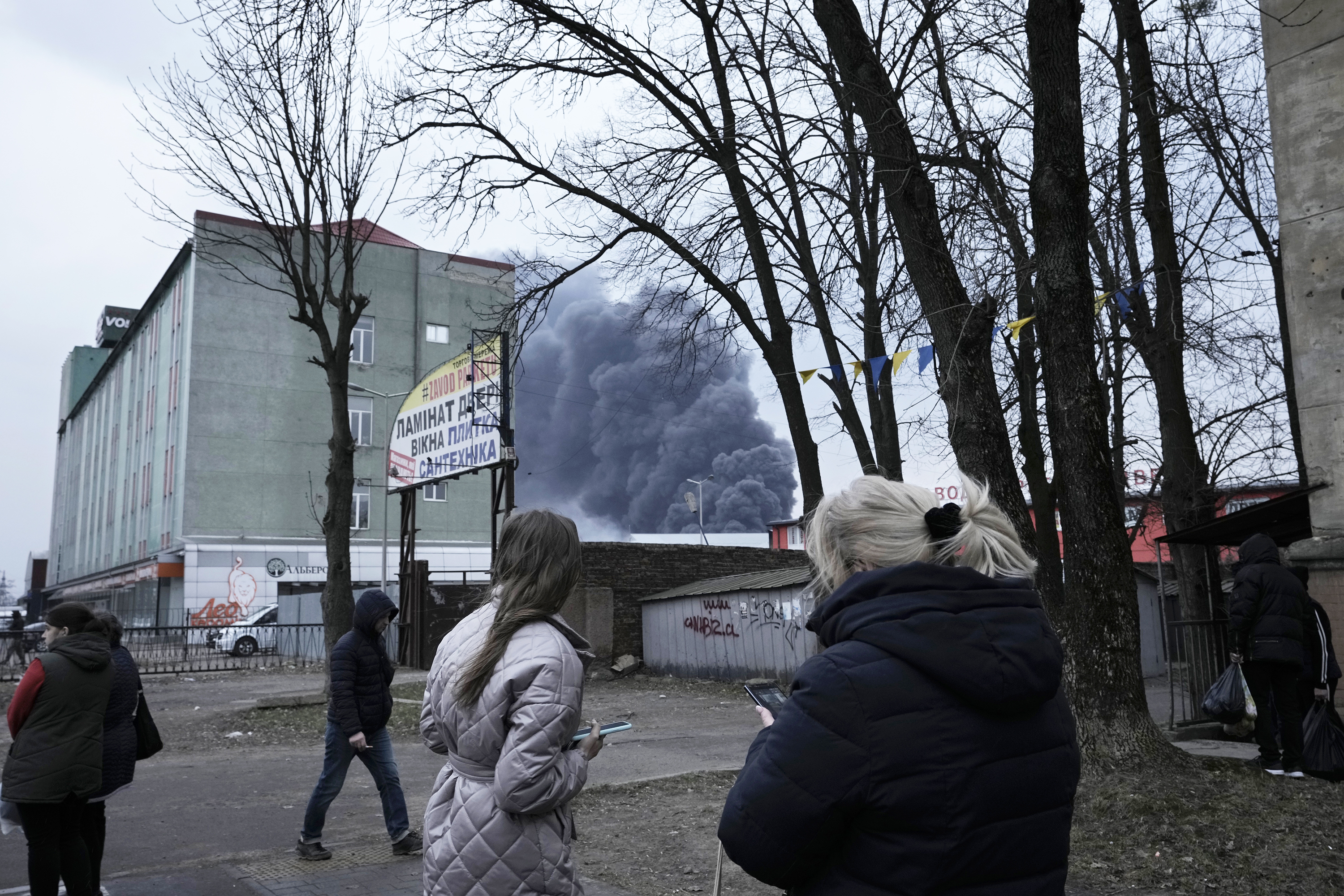 3月26日星期六，乌克兰利沃夫发生爆炸后，人们看着建筑物后面升起的浓烟。