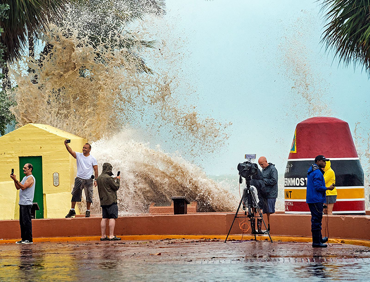 News crews, tourists and local residents take images as high waves from Hurricane Ian crash into the seawall at the Southernmost Point buoy, Tuesday, September 27, in Key West, Florida.