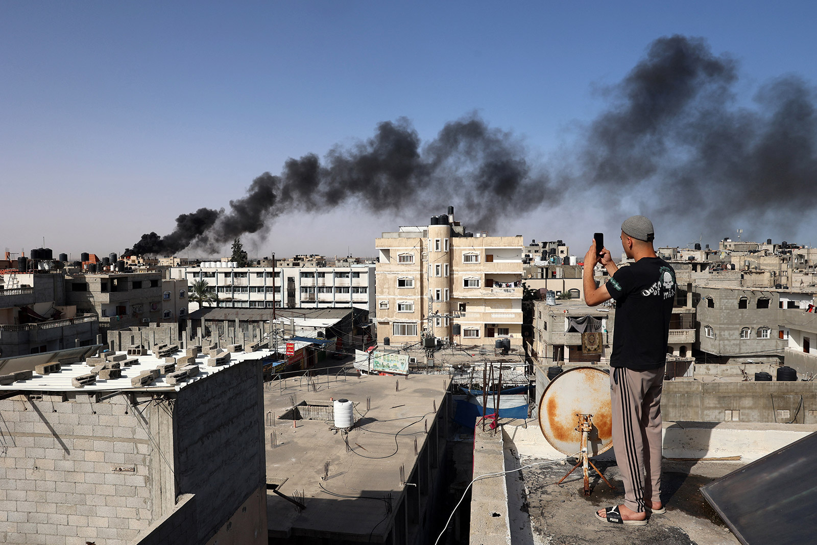 A man snaps pictures from a rooftop as thick, black smoke rises from a fire in a building caused by Israeli bombardment in Rafah on May 10.