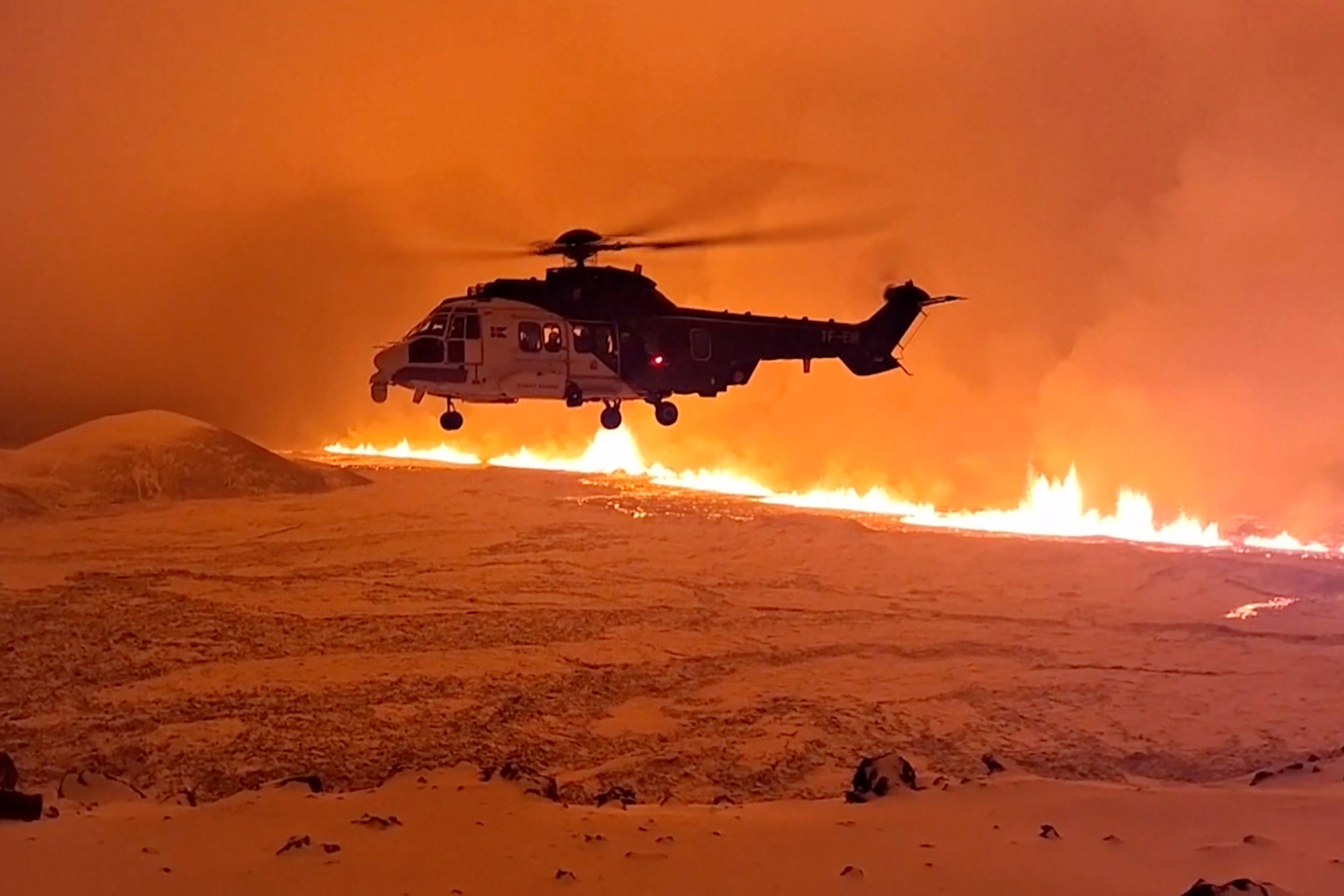 A helicopter with the Icelandic Coast Guard flies by magma running on a hill near Grindavik late Monday.