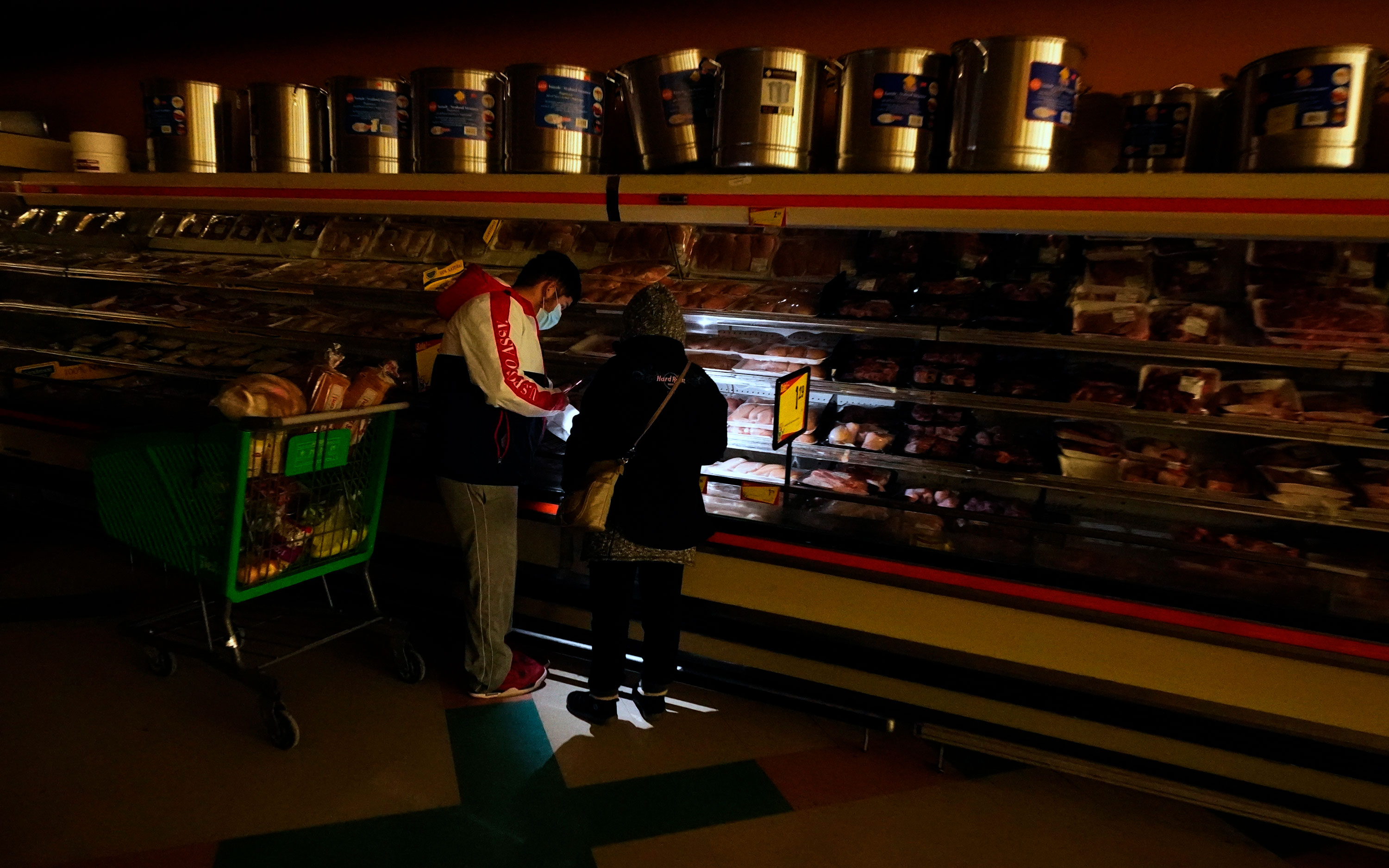 Customers use the light from a cell phone to look in the meat section of a grocery store on February 16 in Dallas, Texas.